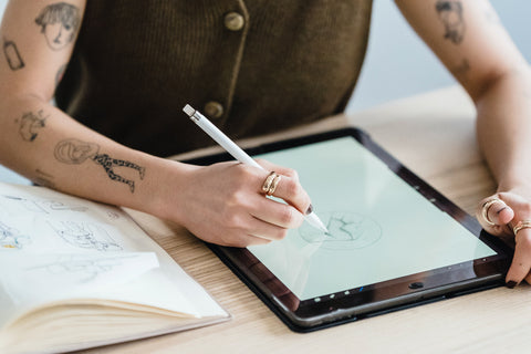 A person with tattoos doodles on a tablet