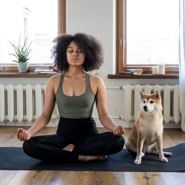 A woman and her dog sit on a yoga mat