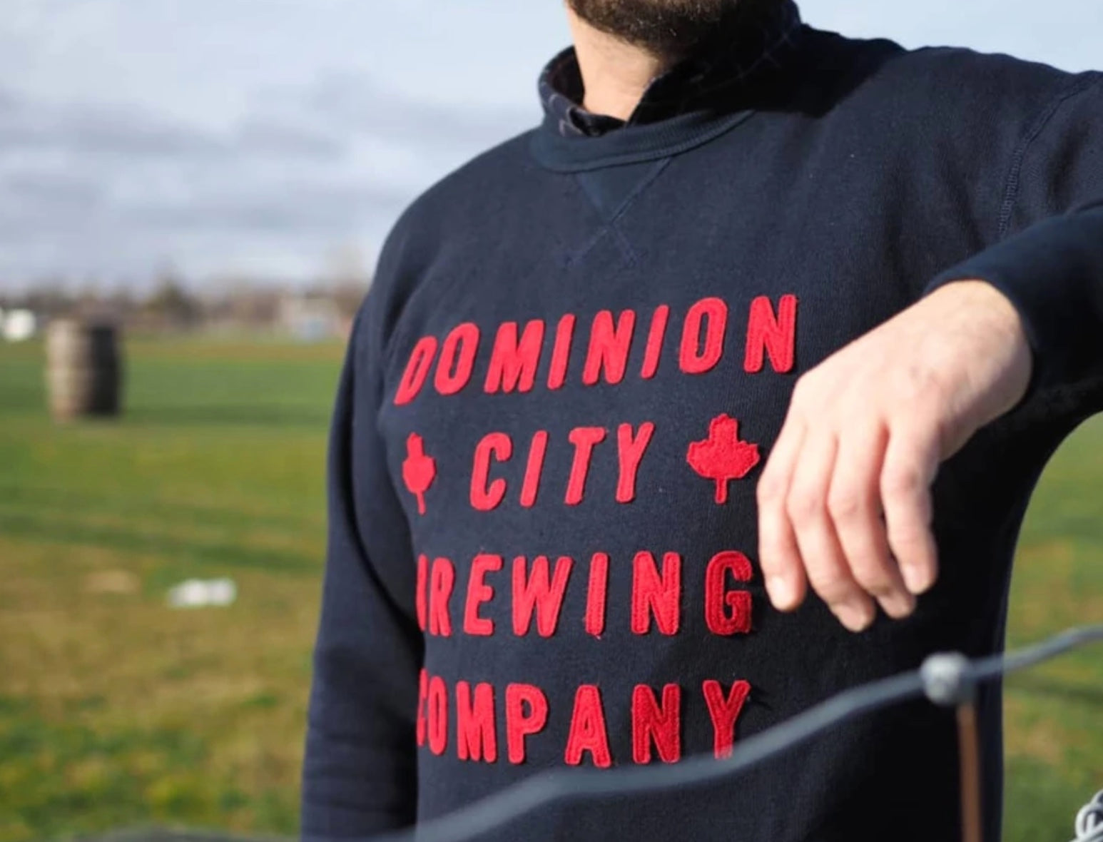 Ein Mann mit einem Pullover der  Dominion City Brewing Company auf einem Feld. Du kannst neben Lebensmitteln auch andere Dinge wie zum Beispiel Merchandise verkaufen.