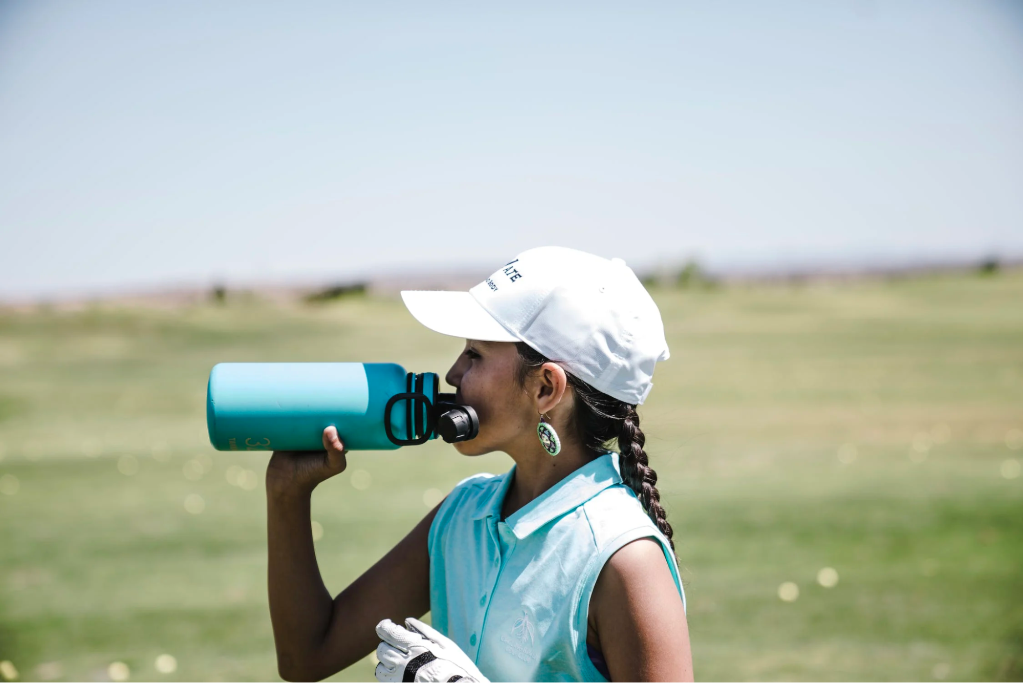 A person drinking from an insulated water bottle while playing a round of golf.