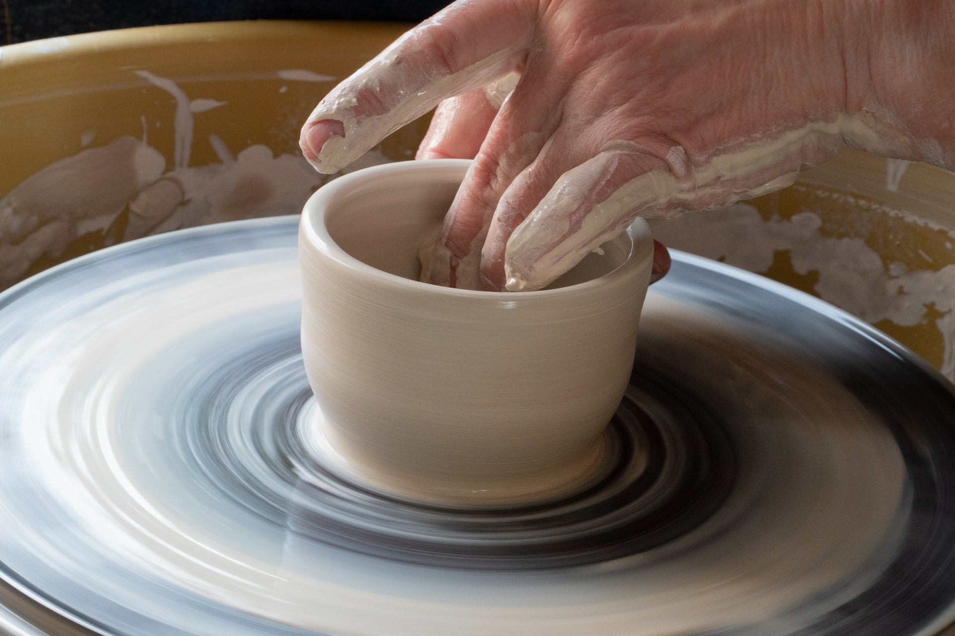 The hands of a ceramicist pinching an object on a wheel.