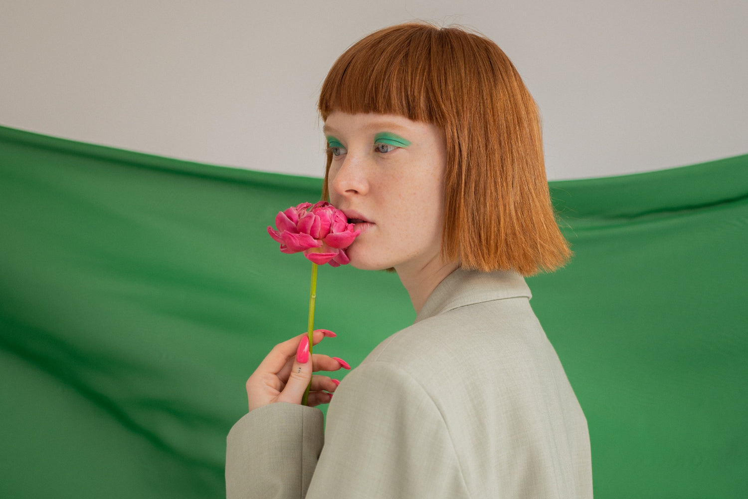 A woman with bangs sniffs a pink flower