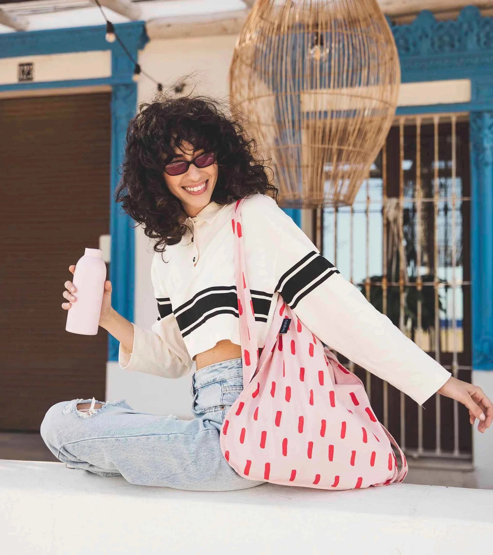 Woman sits on a ledge holding a water bottle and a reusable bag