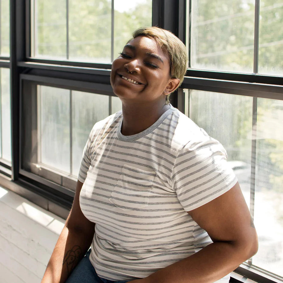 A smiling woman in an eco-friendly t-shirt leans against a large window