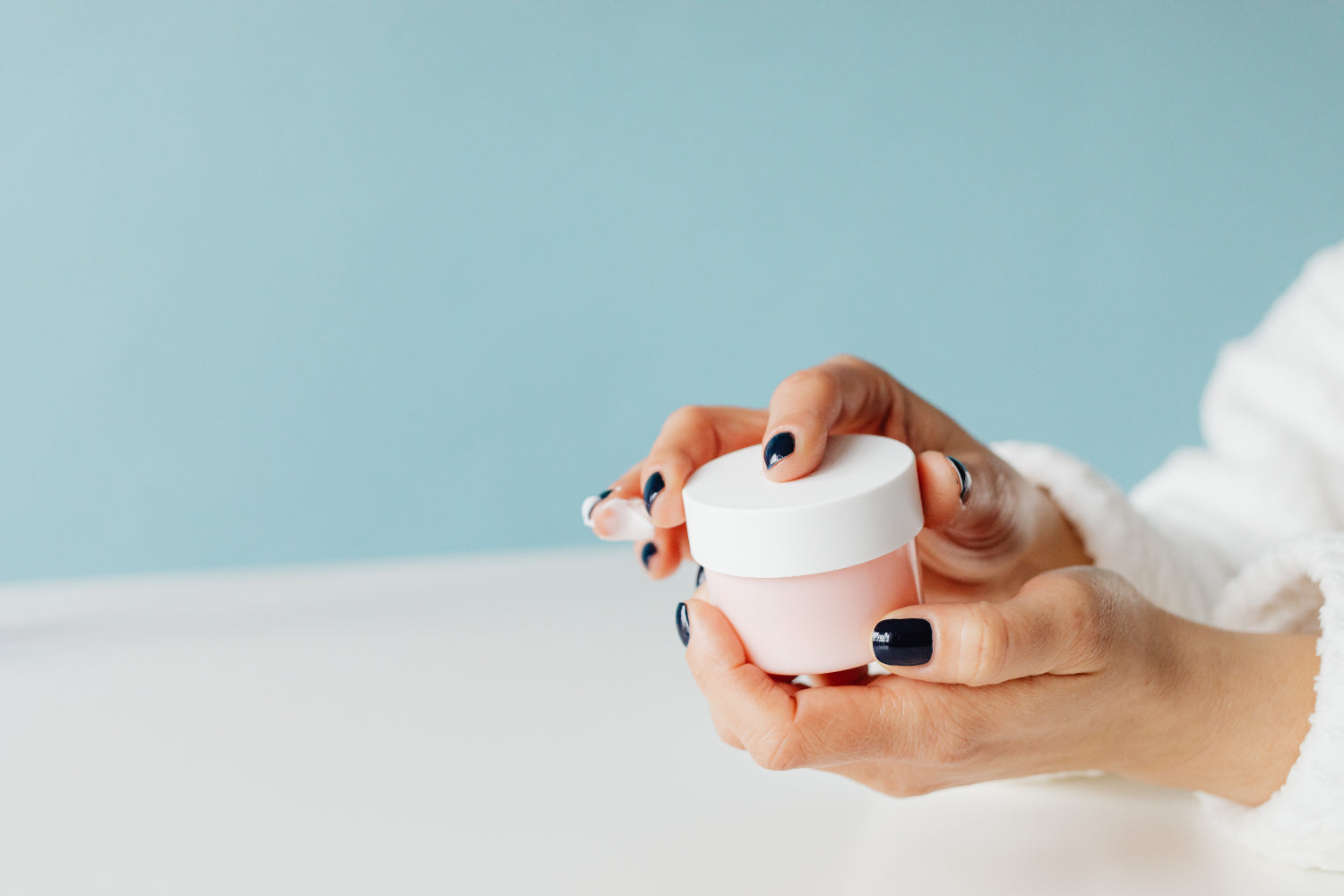 Hands hold an unmarked jar of skin cream