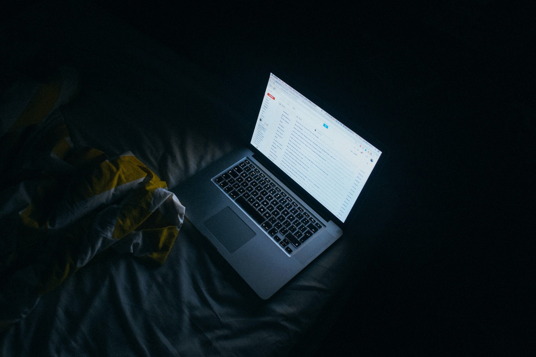 A laptop with the screen turned on on a bed in a dark room