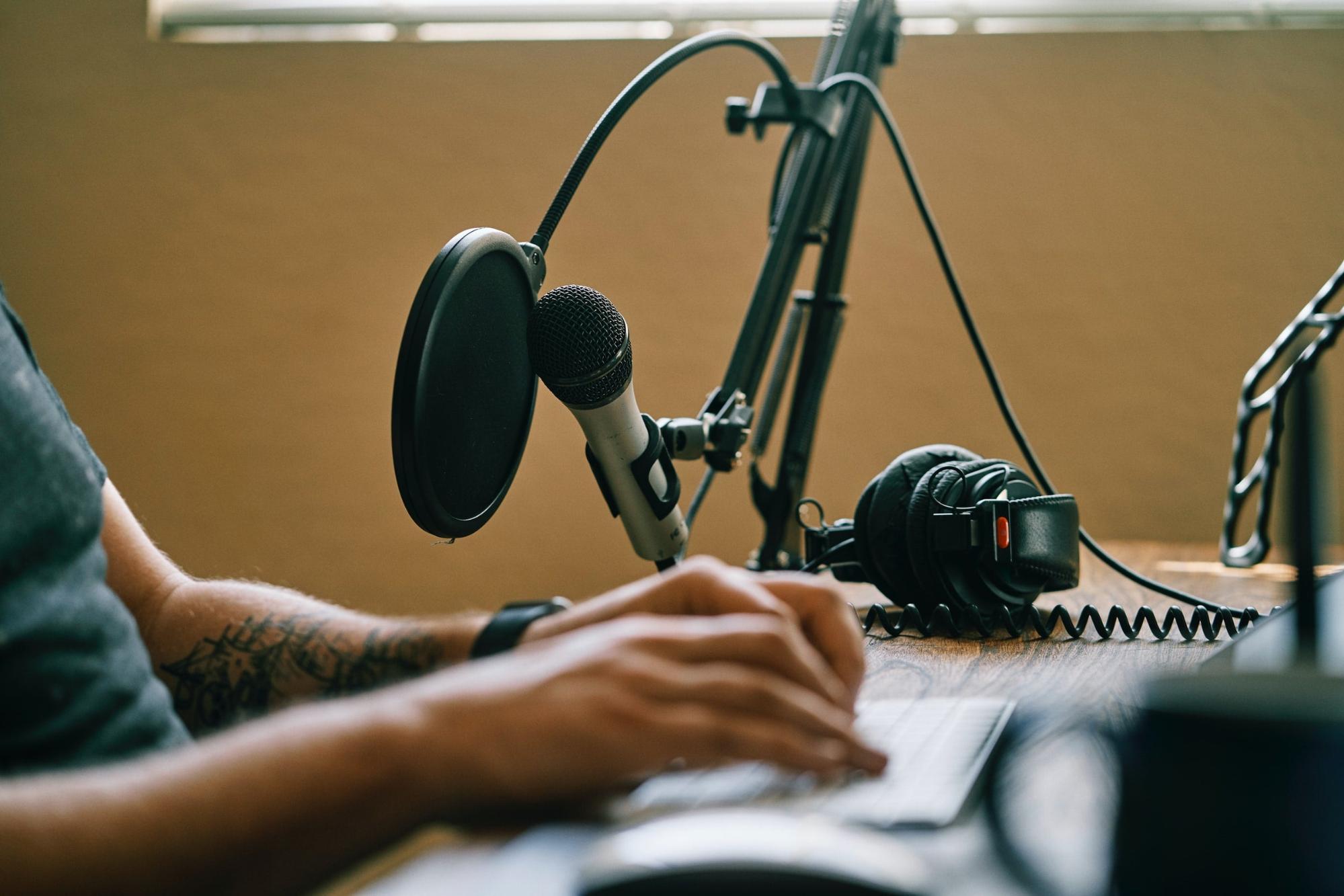 A person sits in front of a microphone and keyboard, editing a podcast