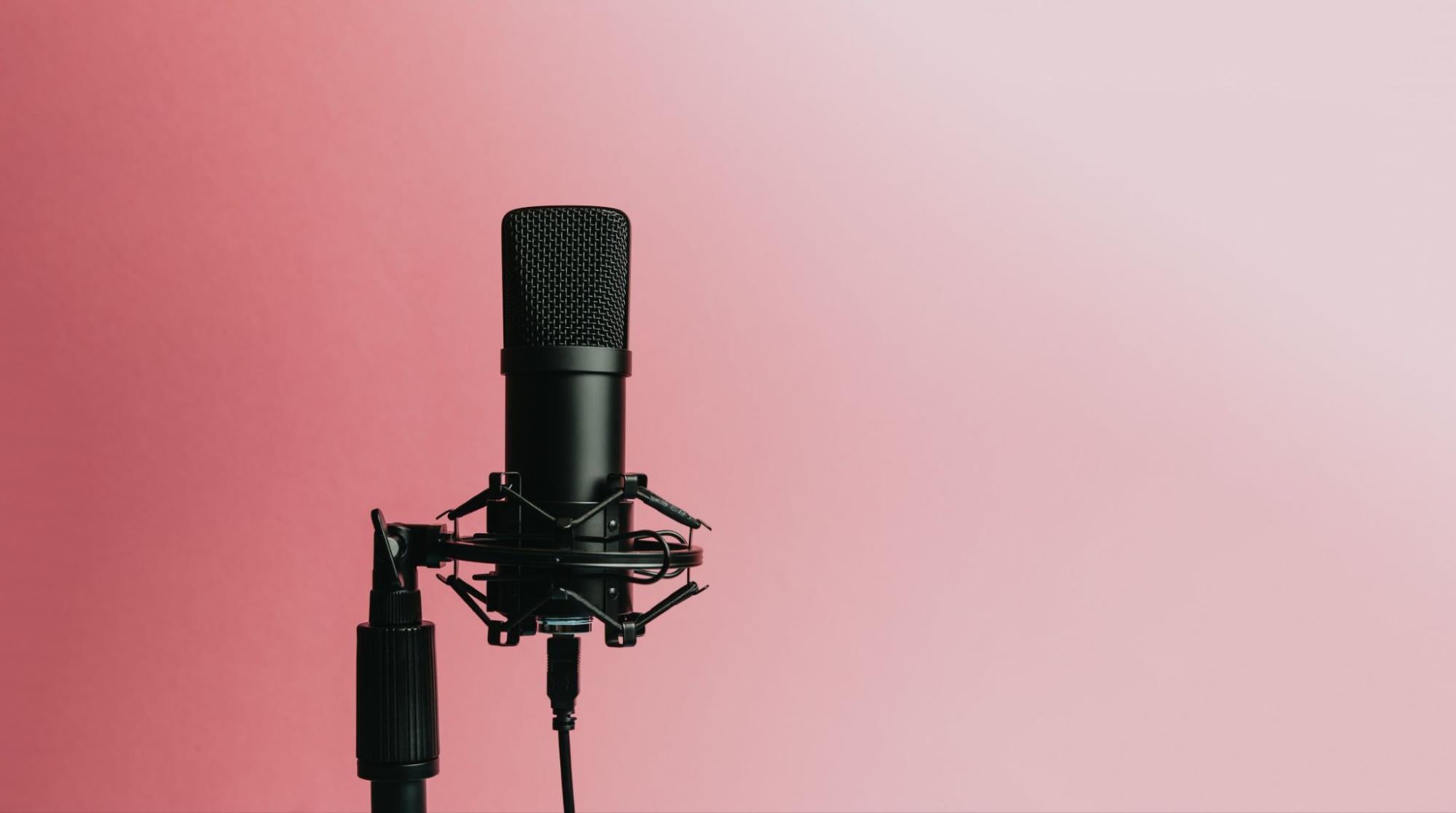 A black microphone is connected to a black stand against a pink background.