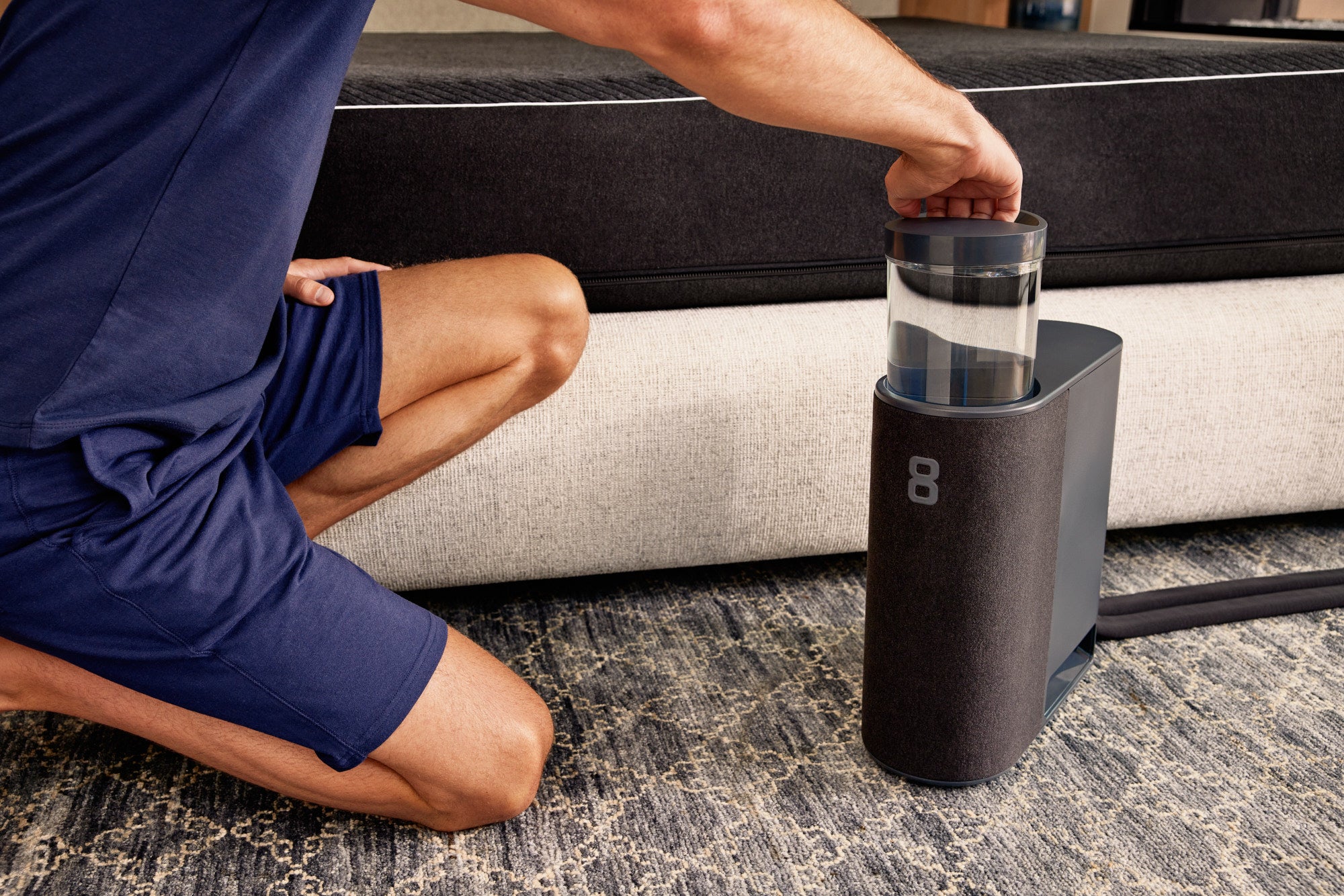 A man kneeling on the floor next to an Eight Sleep Pod Pro mattress refills the water canister in the Hub.