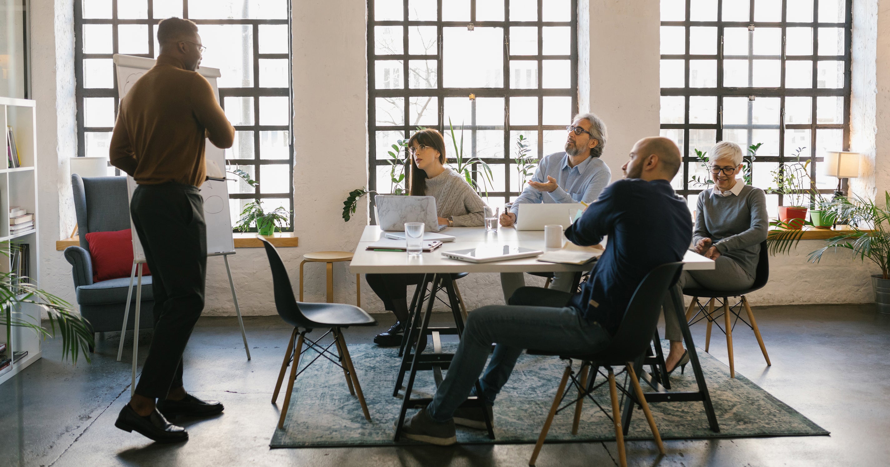 Afbeelding van een persoon die staat en een elevator pitch geeft aan vier mensen die aan een tafel zitten