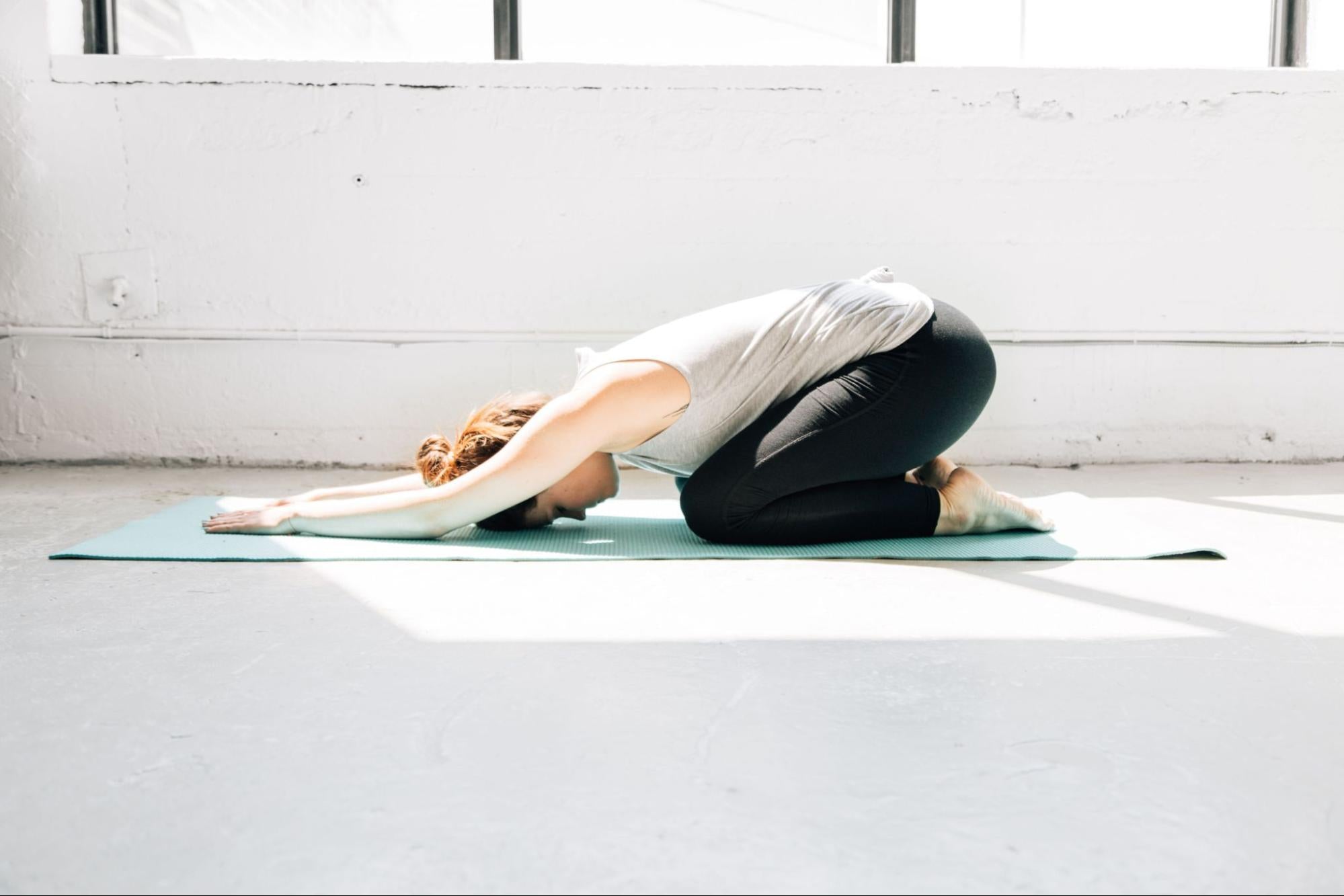 A model in yoga clothing resting in a child’s pose on a yoga mat. 