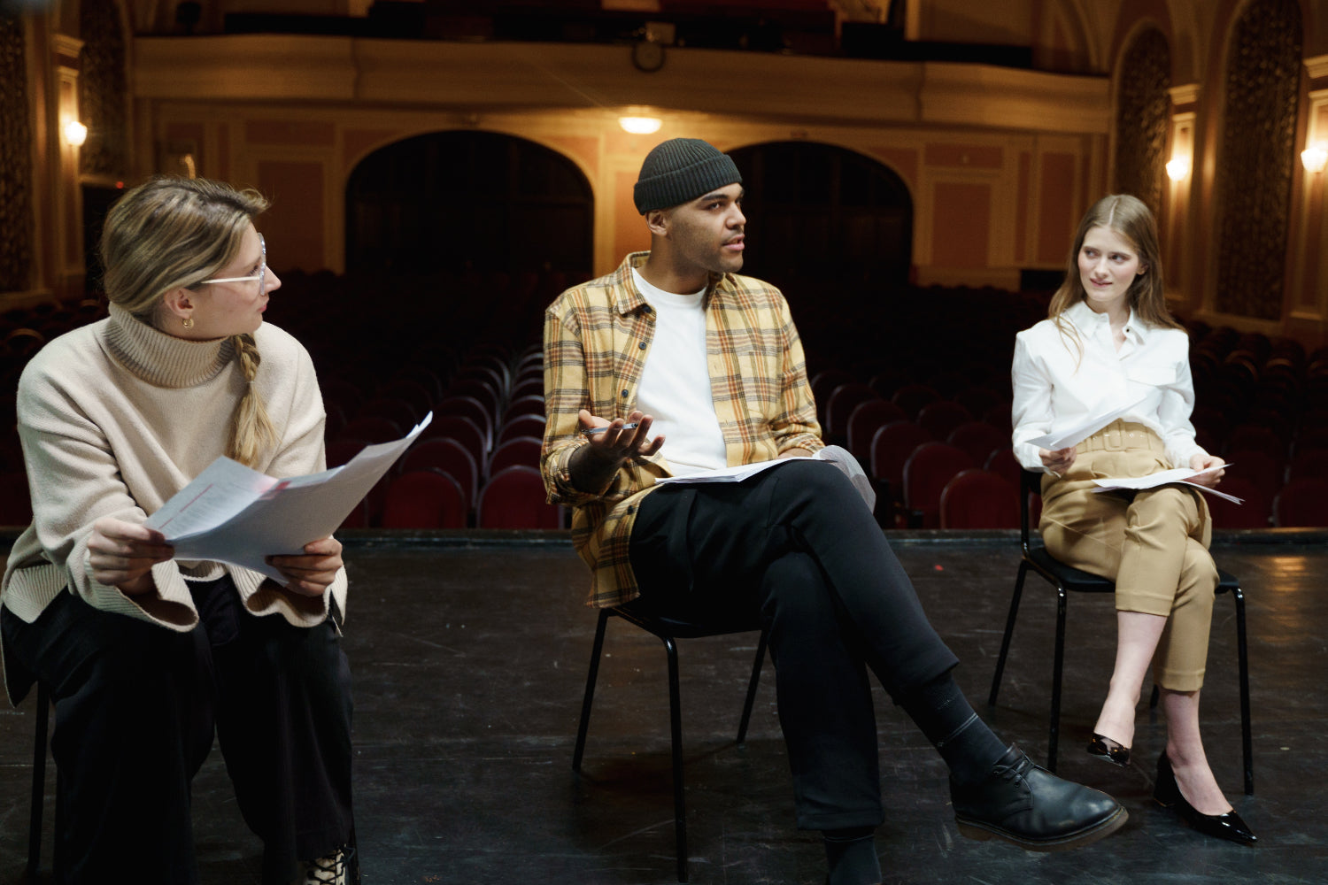 Three people sit in a theatre setting discussing a script