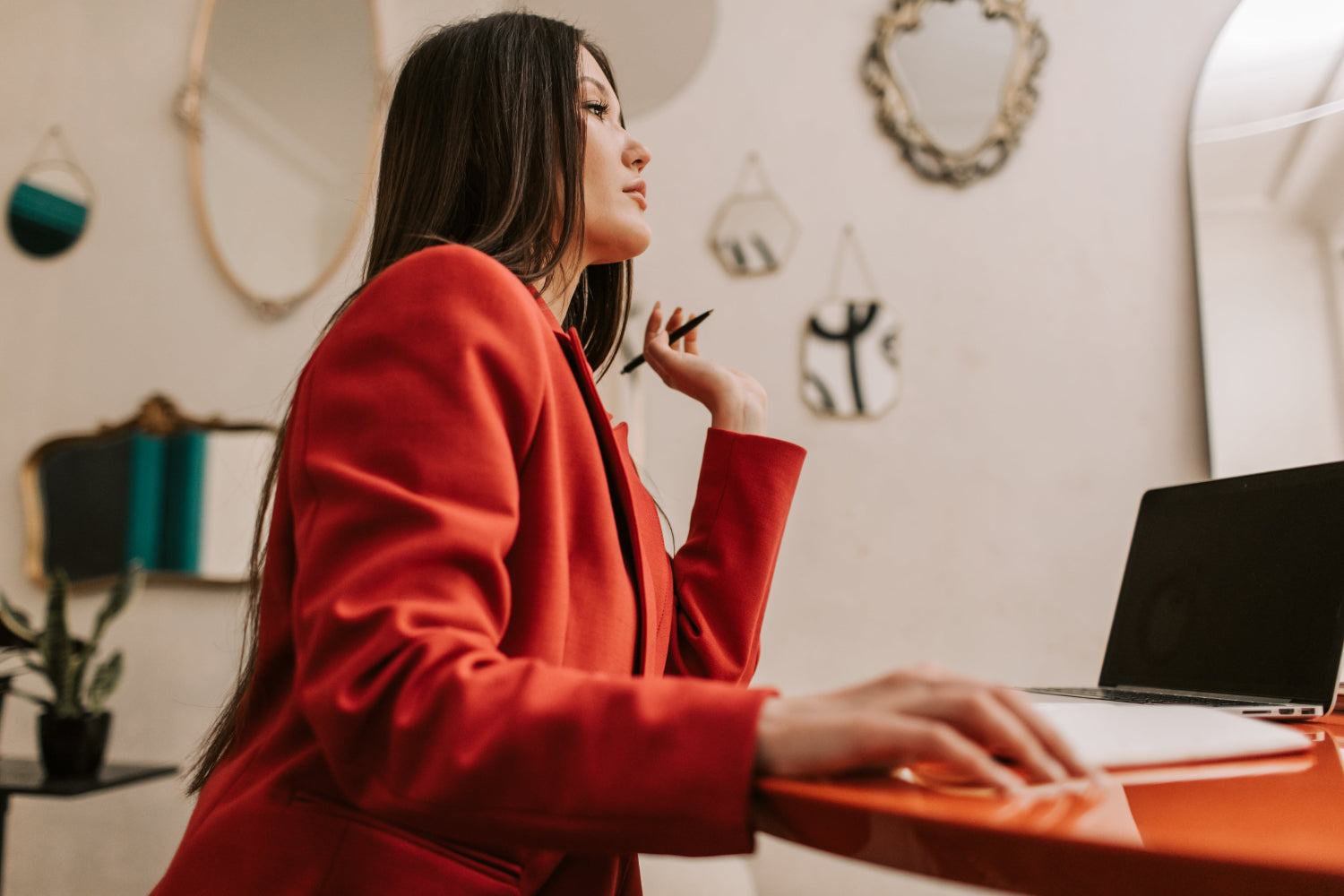 Woman in a blazer sits at a computer desk thinking