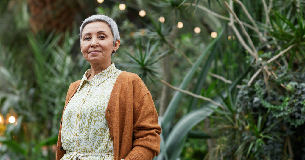 Older woman stands outside under a canopy of greenery and lights