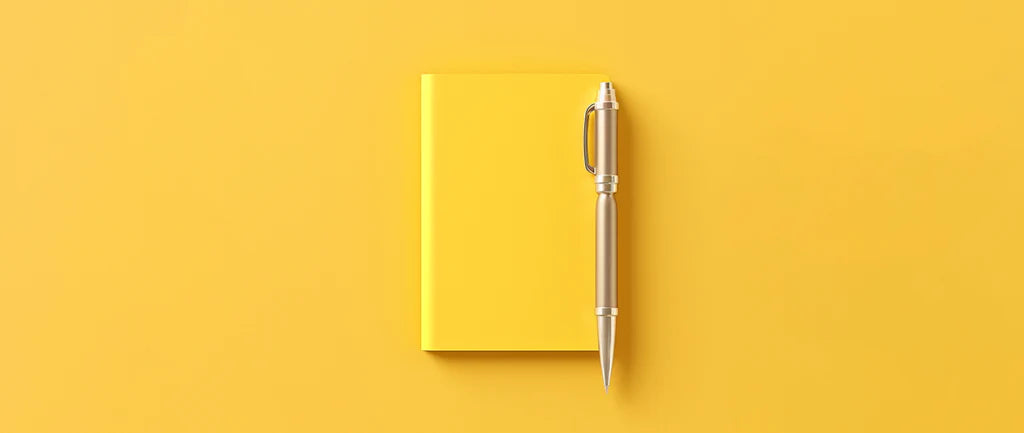 A yellow notebook and pen sit on a yellow plain background