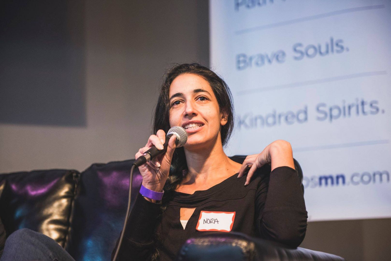 Portrait of Nora Rahimian speaking into a microphone on stage at an event