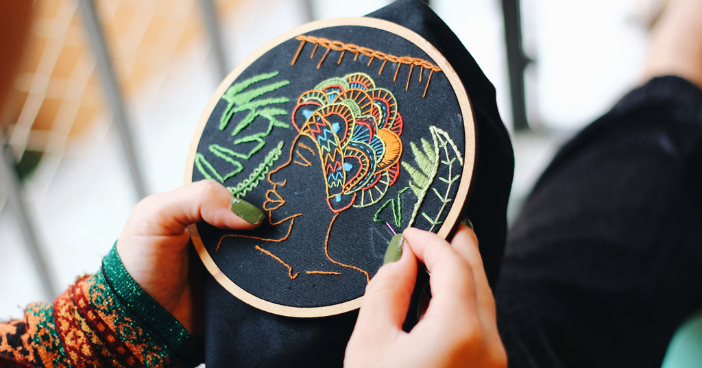 在刺绣箍上工作的手的特写，在黑色的背景上用彩色的线创造一个人的设计