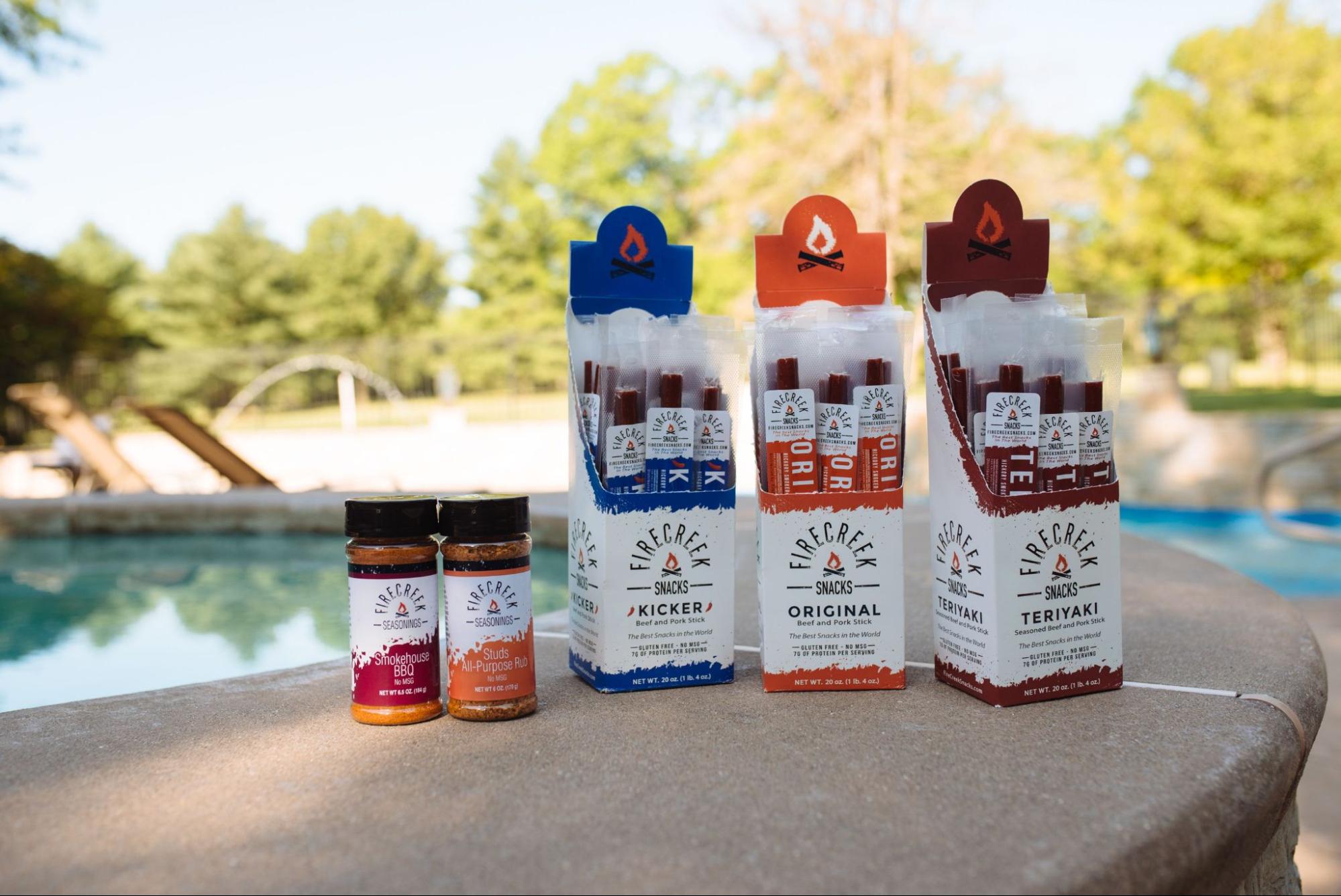 A selection of seasonings and jerky from FireCreek Snacks backdropped by a pool setting.