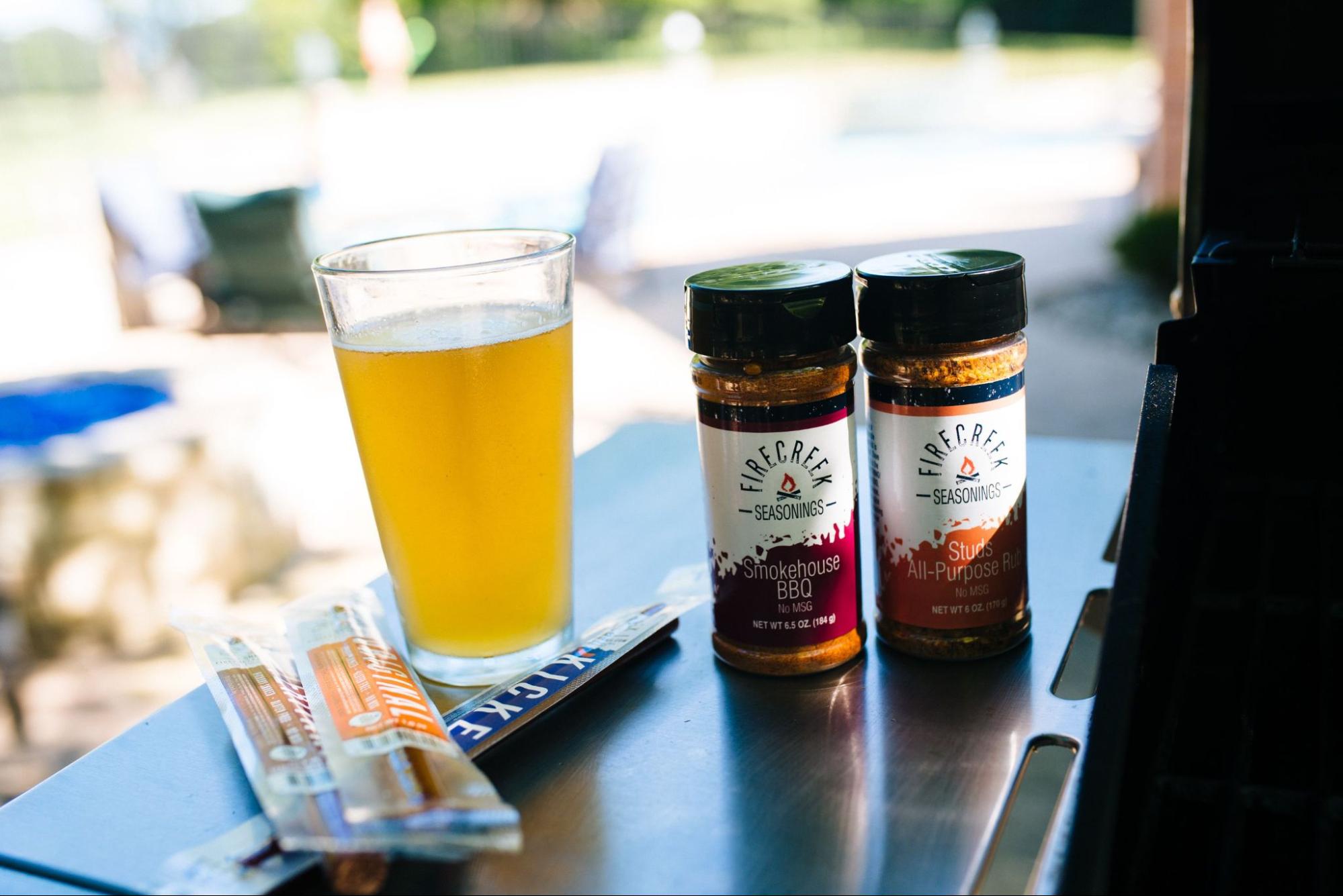 A duo of seasonings from FireCreek and some packs of jerky back dropped by a beverage.