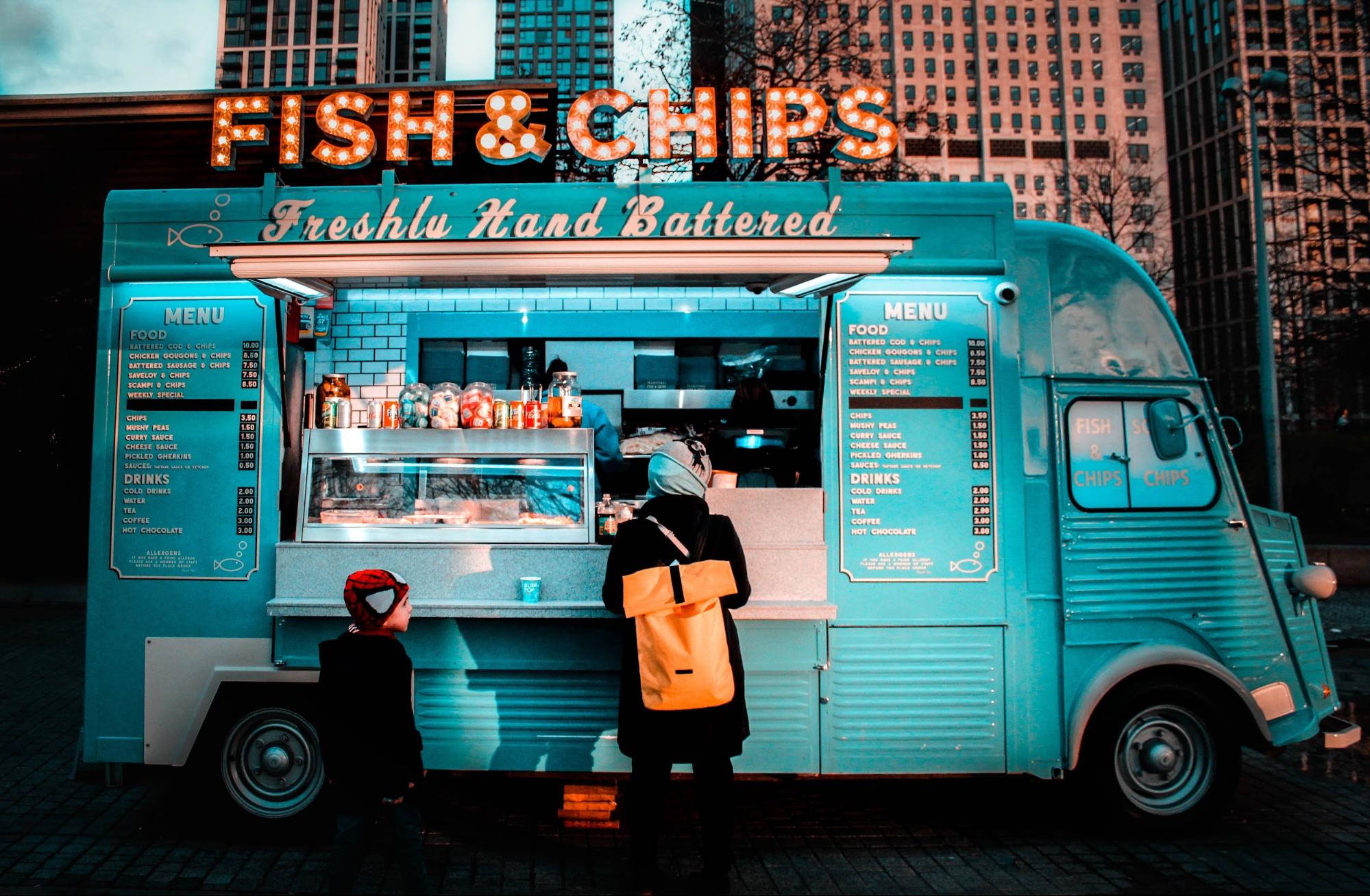 A fish and chips food truck with a customer against city background