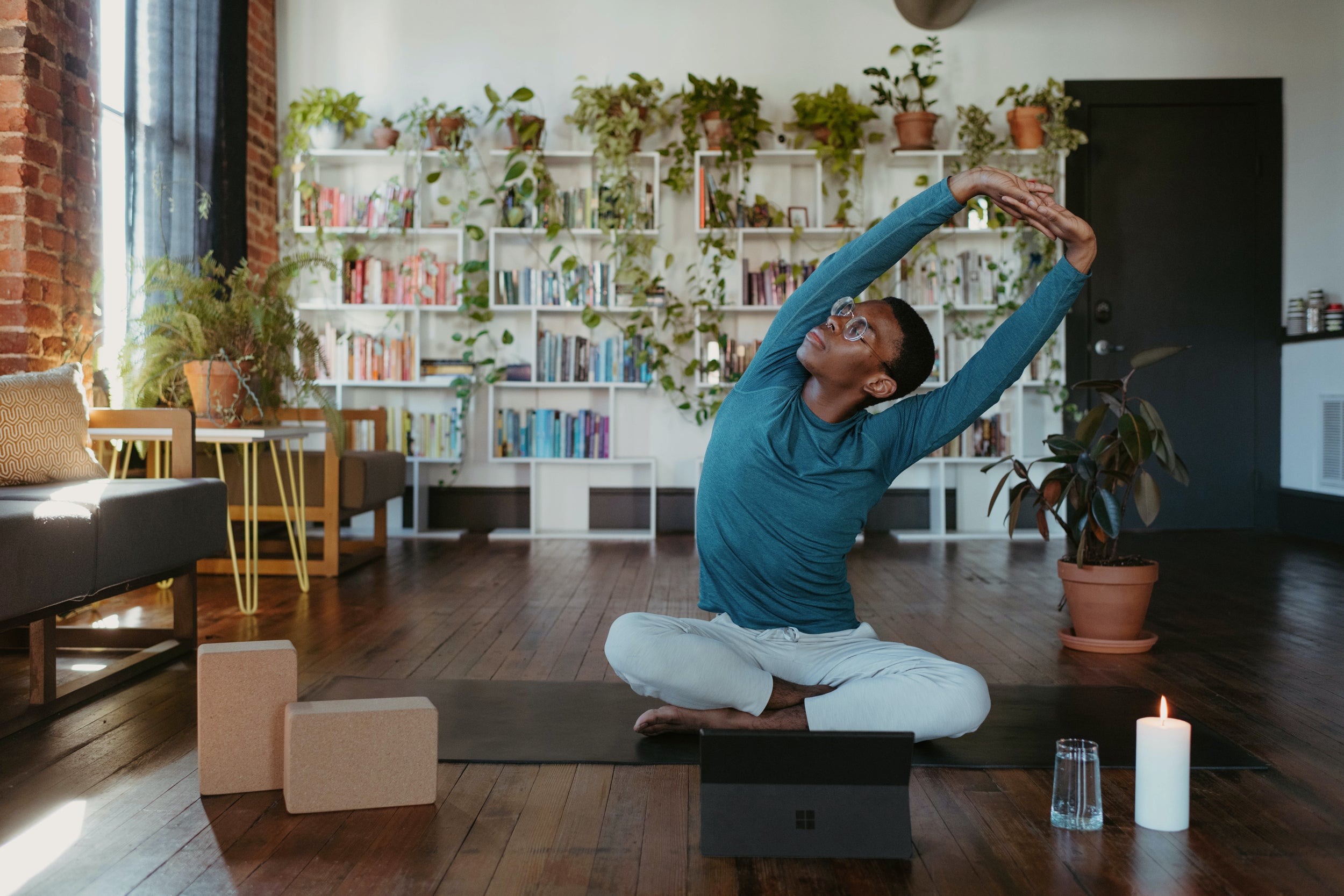 A person sits on a yoga mat doing gentle stretches in a living room 