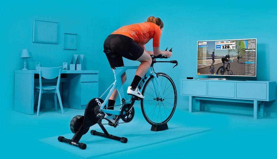 A cyclist rides on a bike with a trainer while participating in a Zwift circuit playing on a TV