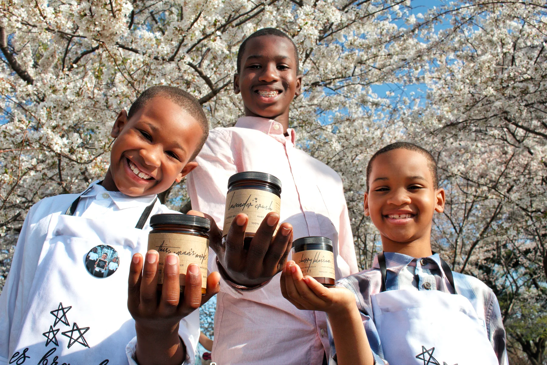 Three young boys holding a brown candle jar in front of a blossom tree.