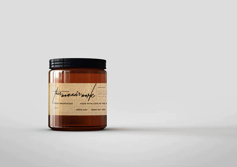 Amber glass candle jar with black lid and handwritten-style label on a light grey background.