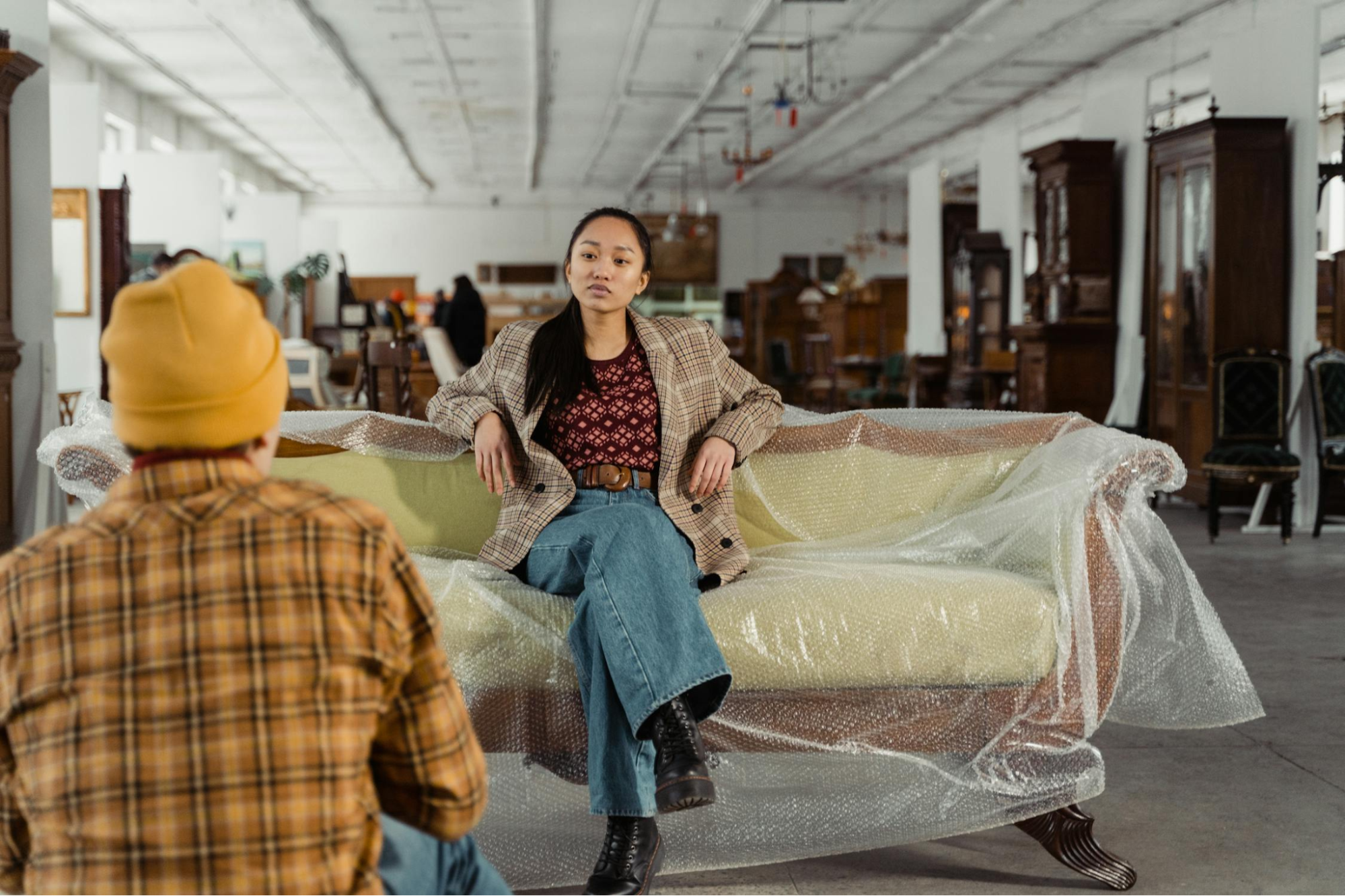 Two people shop for a vintage couch in a used furniture warehouse.