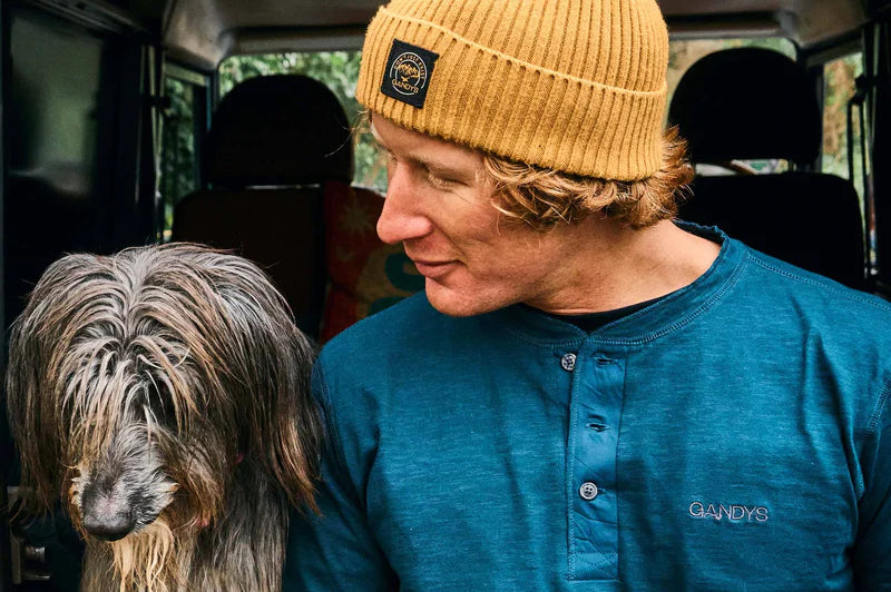 A man in a beanie cap pets a shaggy dog