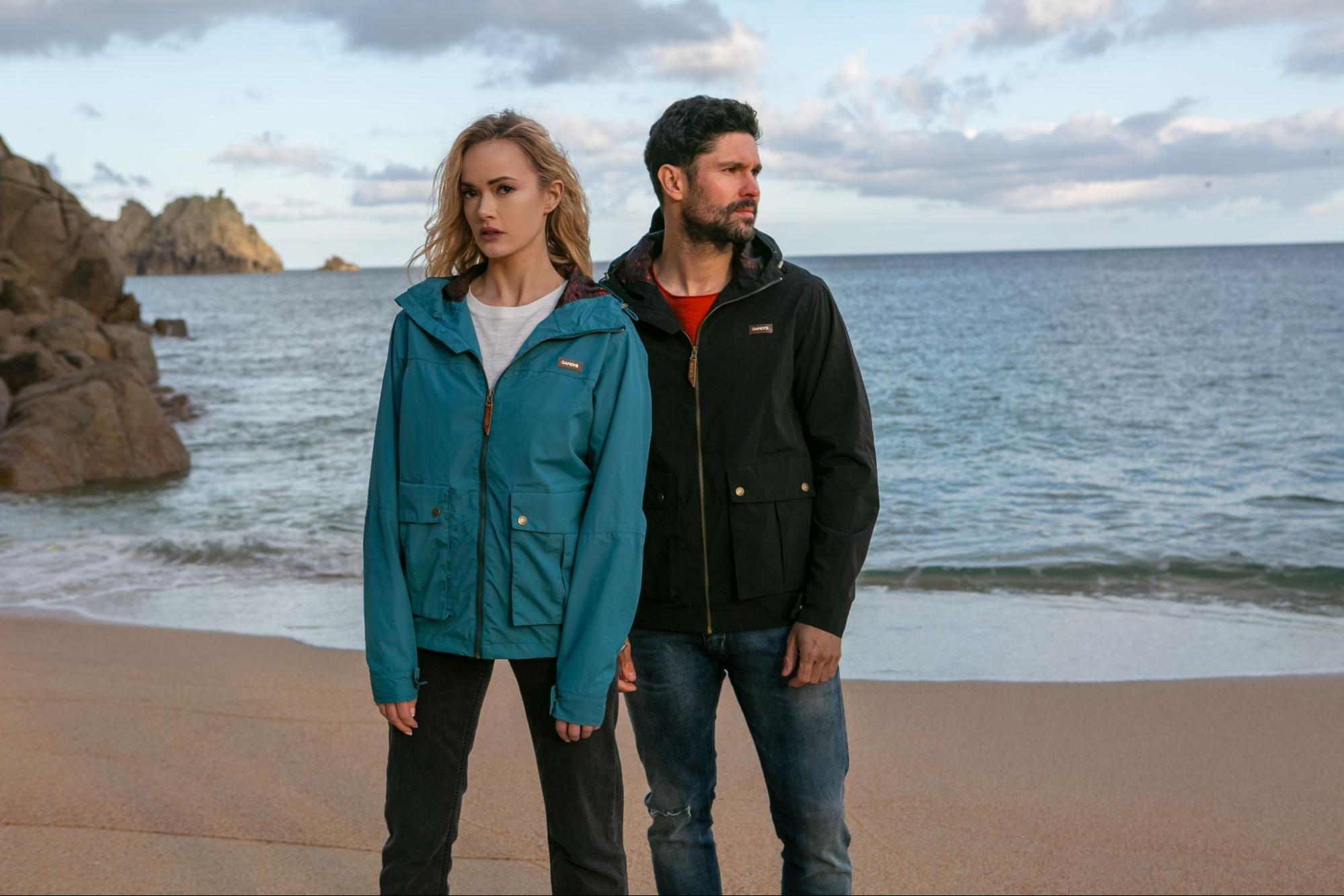 A pair of models in Gandys clothing on a beach setting backdropped by mountains. 