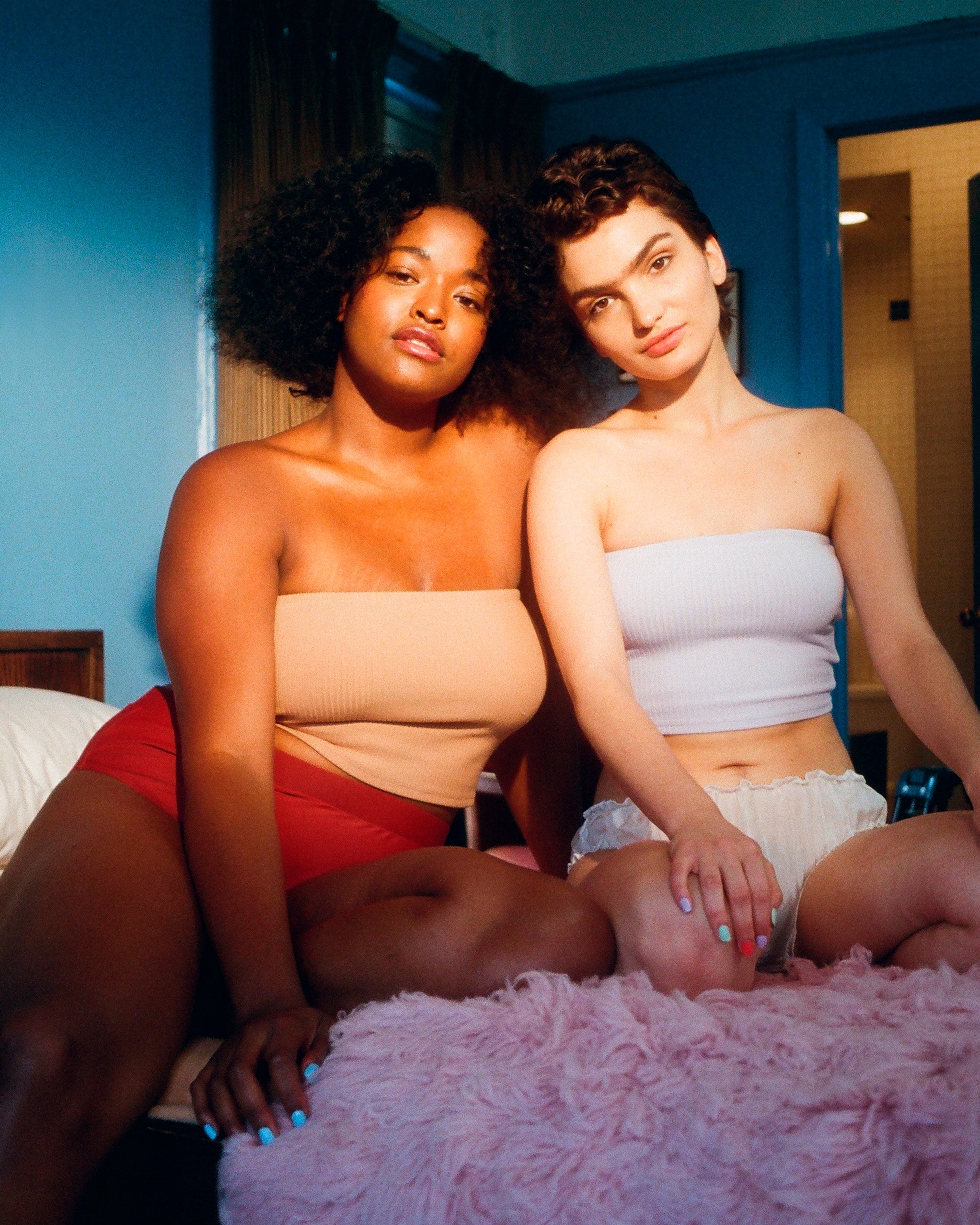 Two women sit on bed inside room