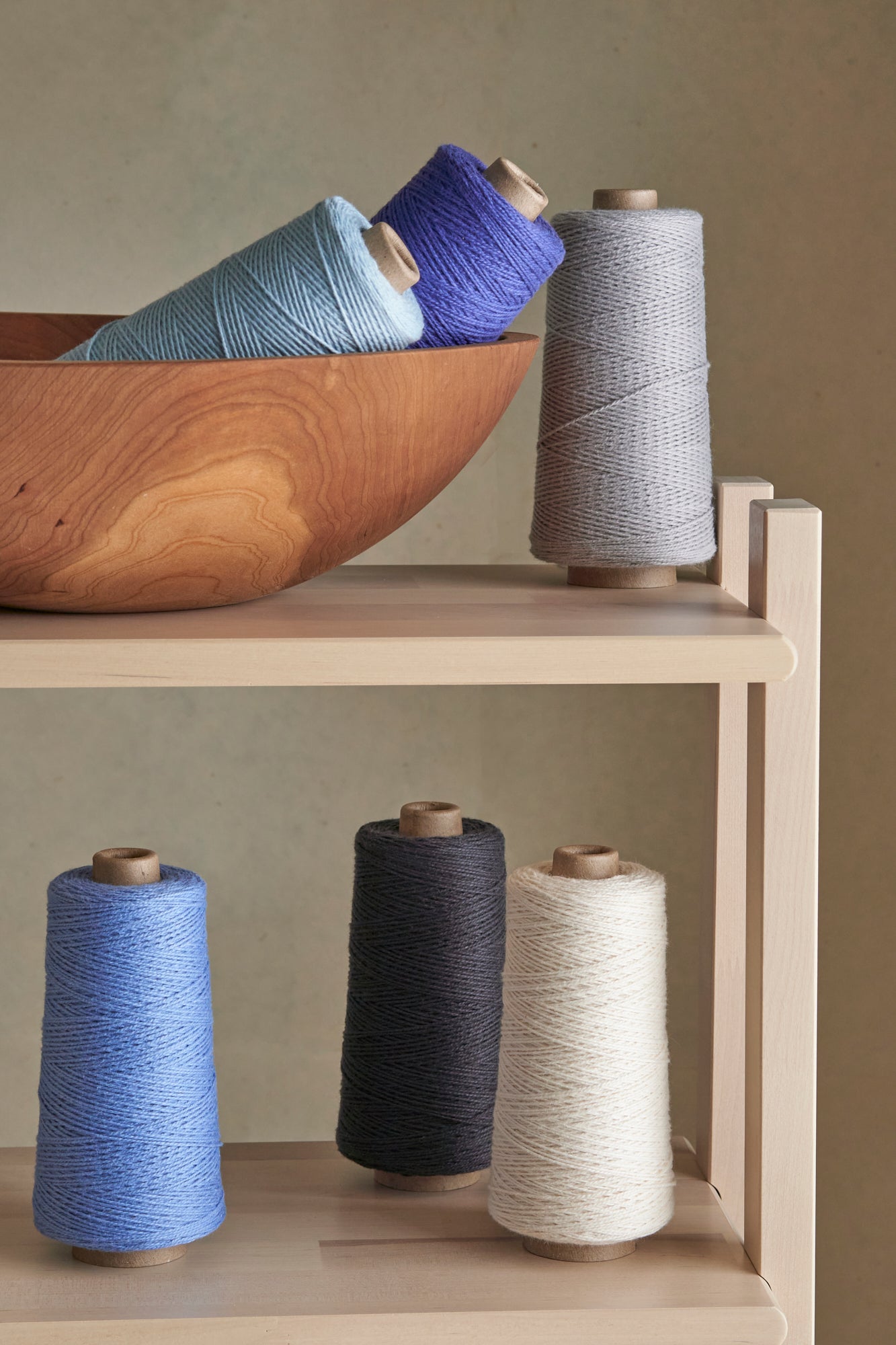 A set of cool toned yarns displayed on a wooden shelf.