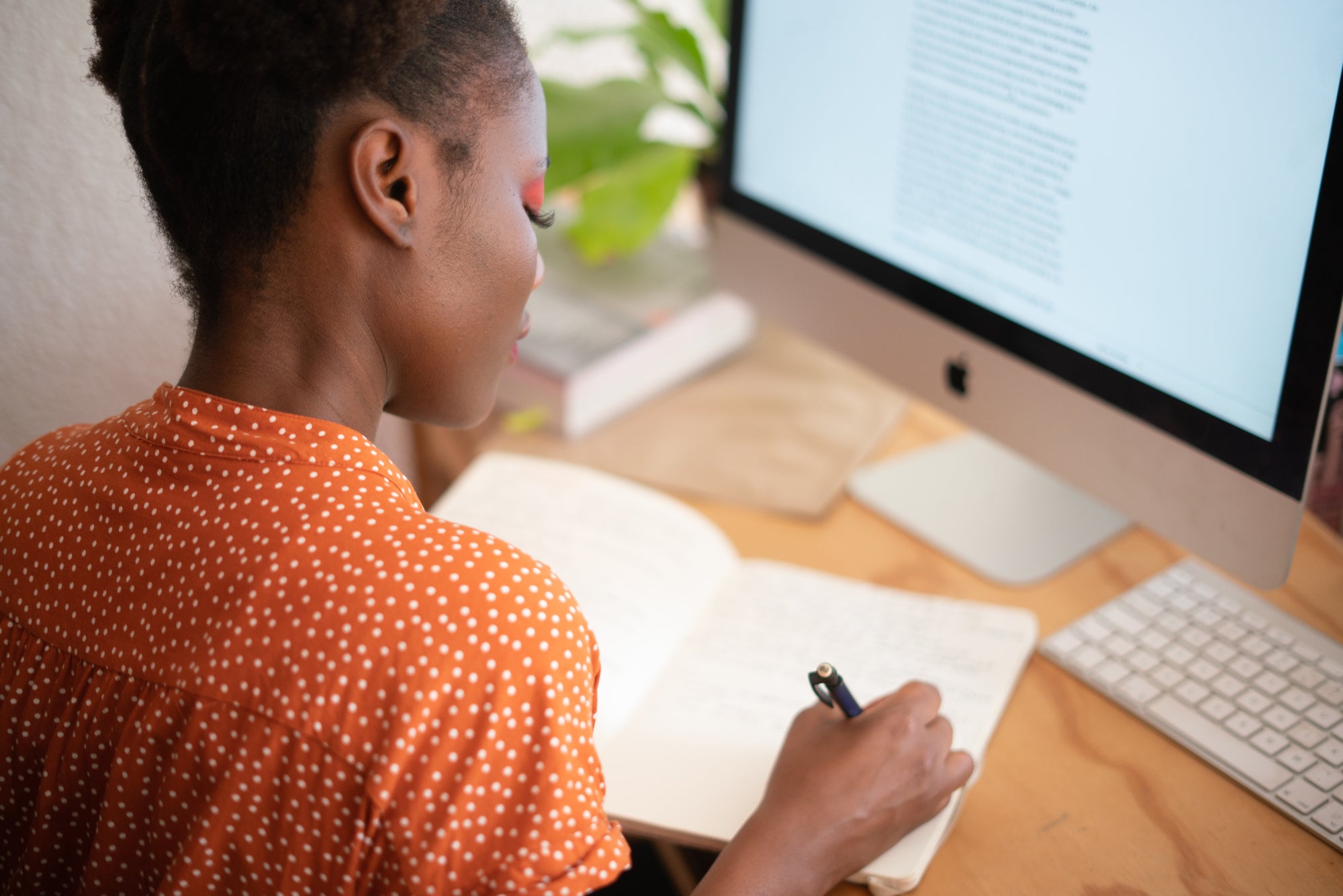 Person writes in a note book while sitting at a desk with a computer