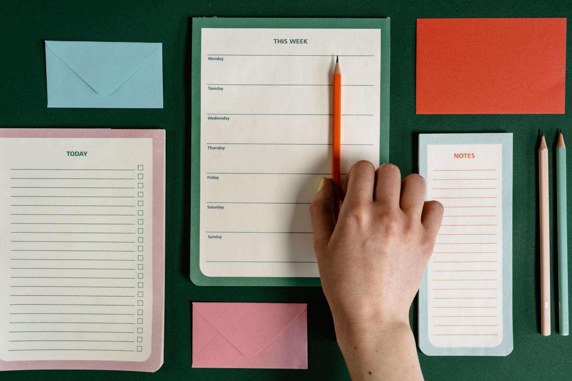 Flatlay of notepads and pencils. A hand reaches into the frame to pick up a pencil