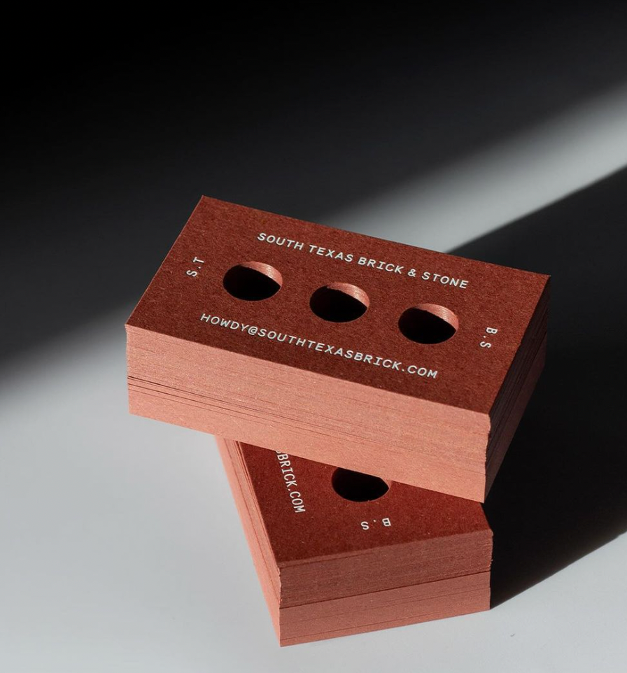 Business card that looks like a brick with three holes cut in the center of the design.