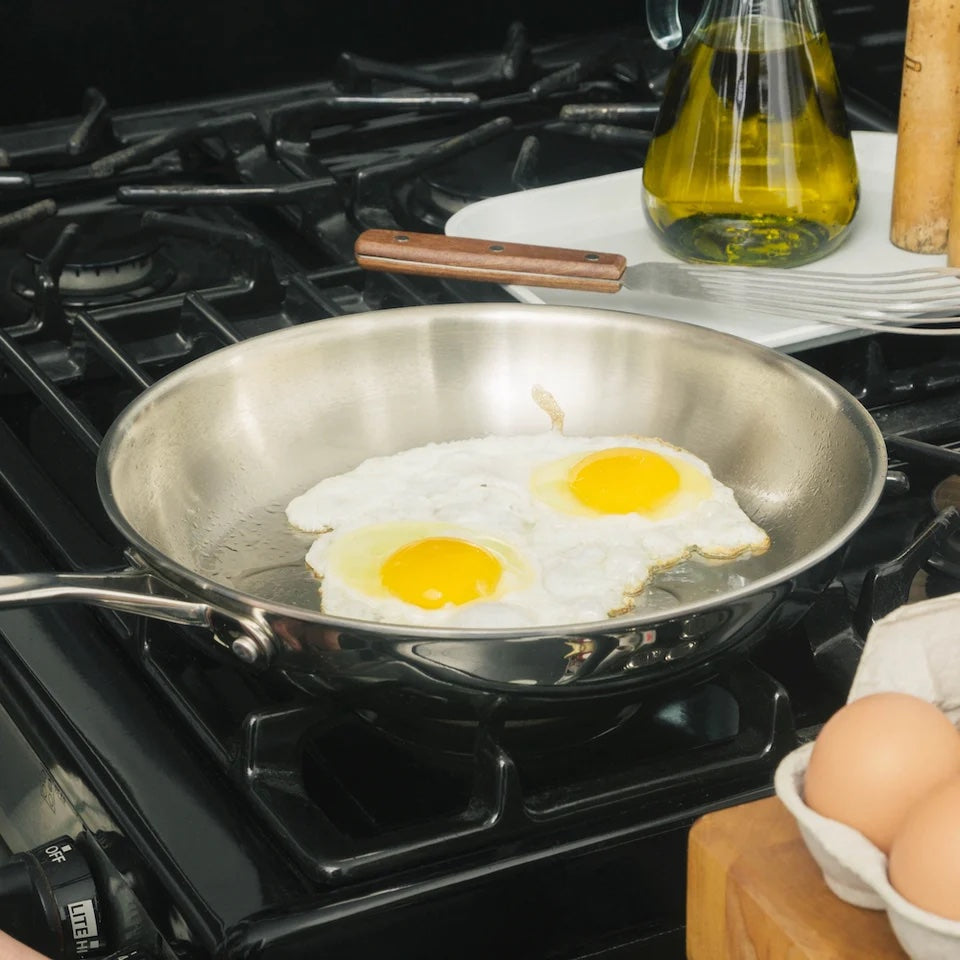 Large stainless steel skillet on a stovetop with two sunny-side up eggs.