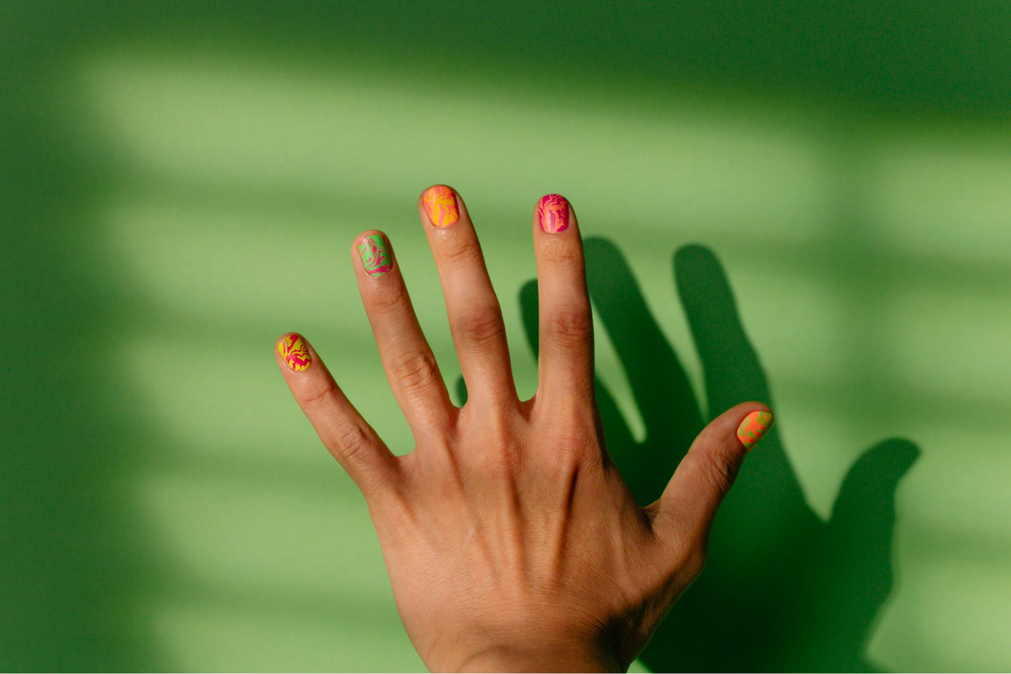 Left hand with intricately painted nails is held up to the light.