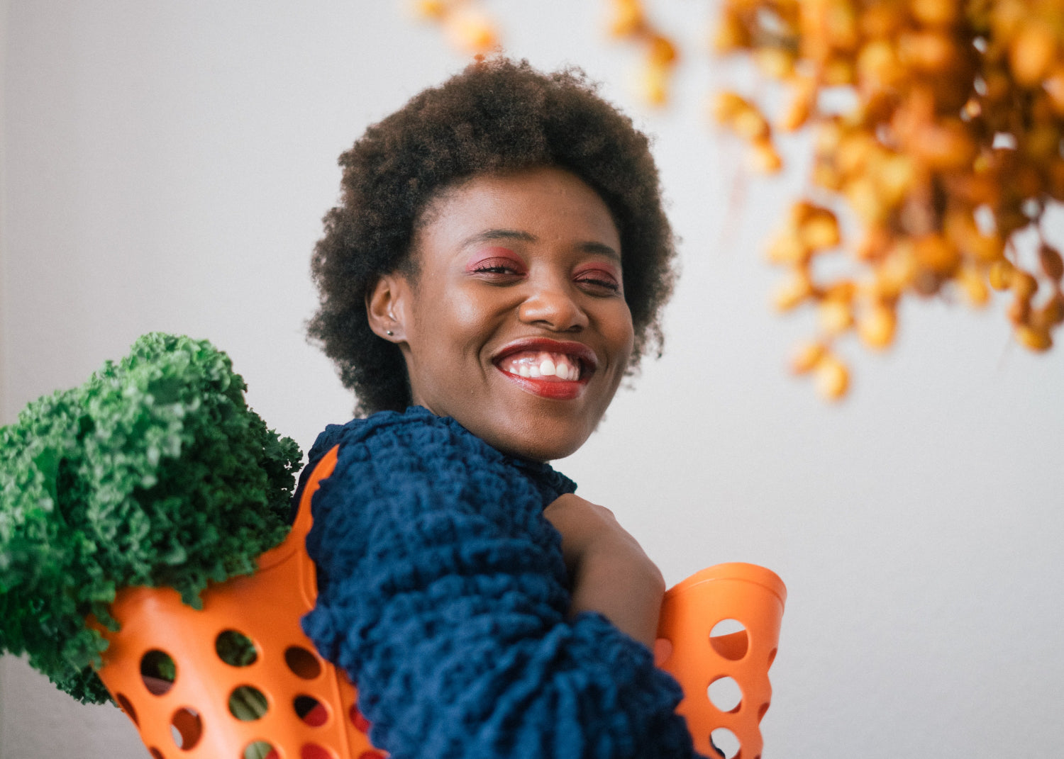 A happy woman carries a plastic basket full of kale