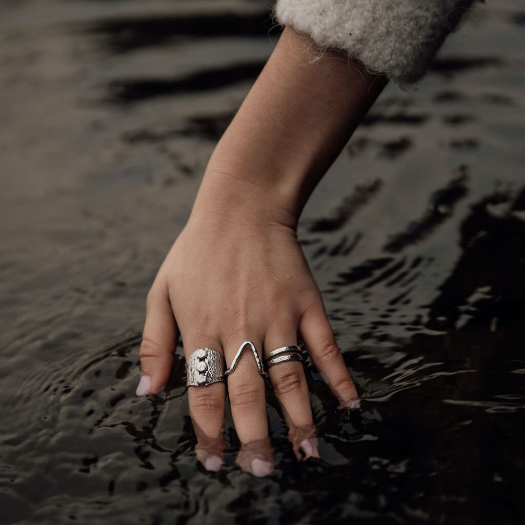 Eine Frau hält ihre mit silbernen Ringen besetzte Hand ins Wasser. Schmuck herstellen lassen und verkaufen gelingt dir mit einer Menge Kreativität und handwerklichem Geschick von allein.