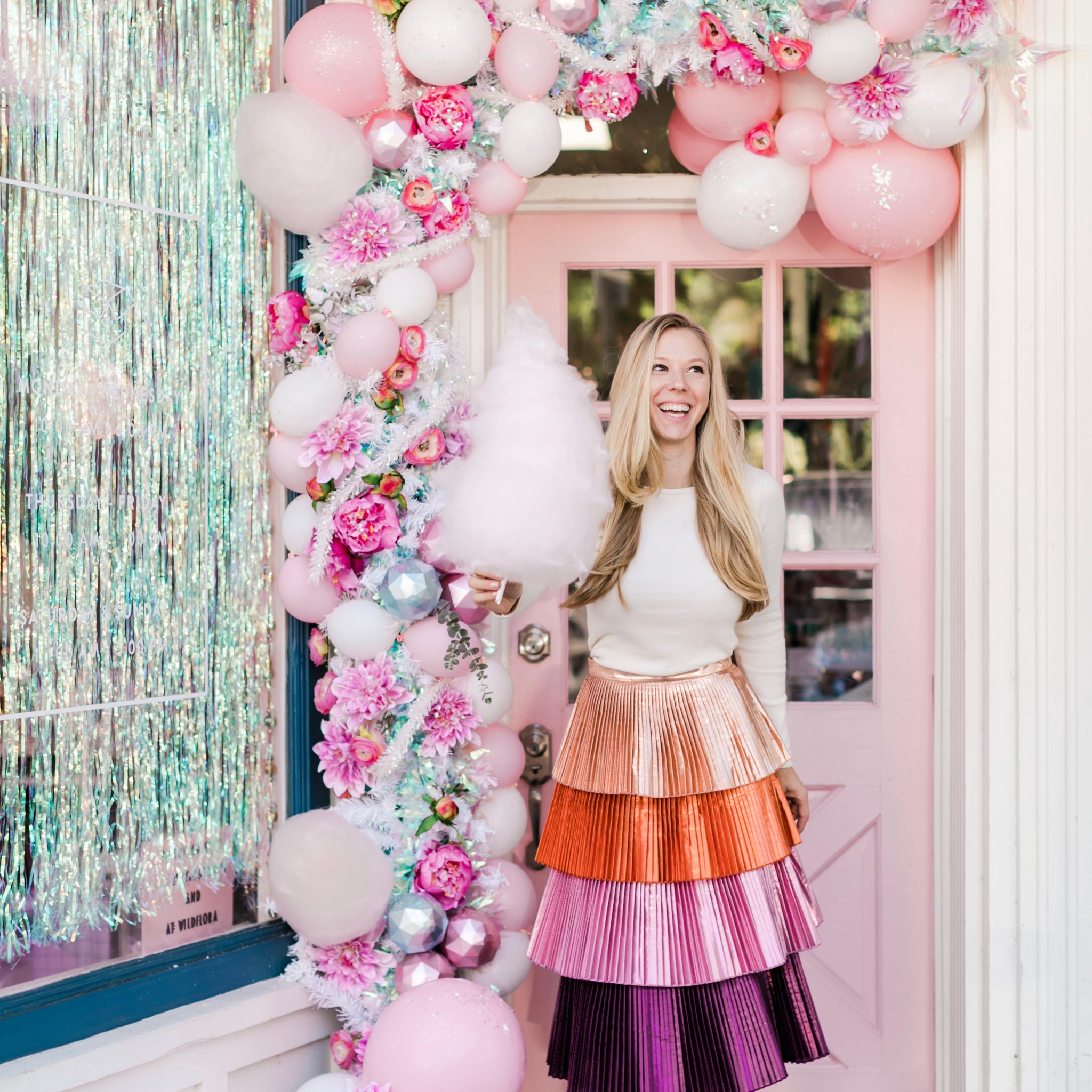 Rachel Huntington, founder of Bonjour Fete holds a cotton candy in front of a pink door decorated with balloons. 