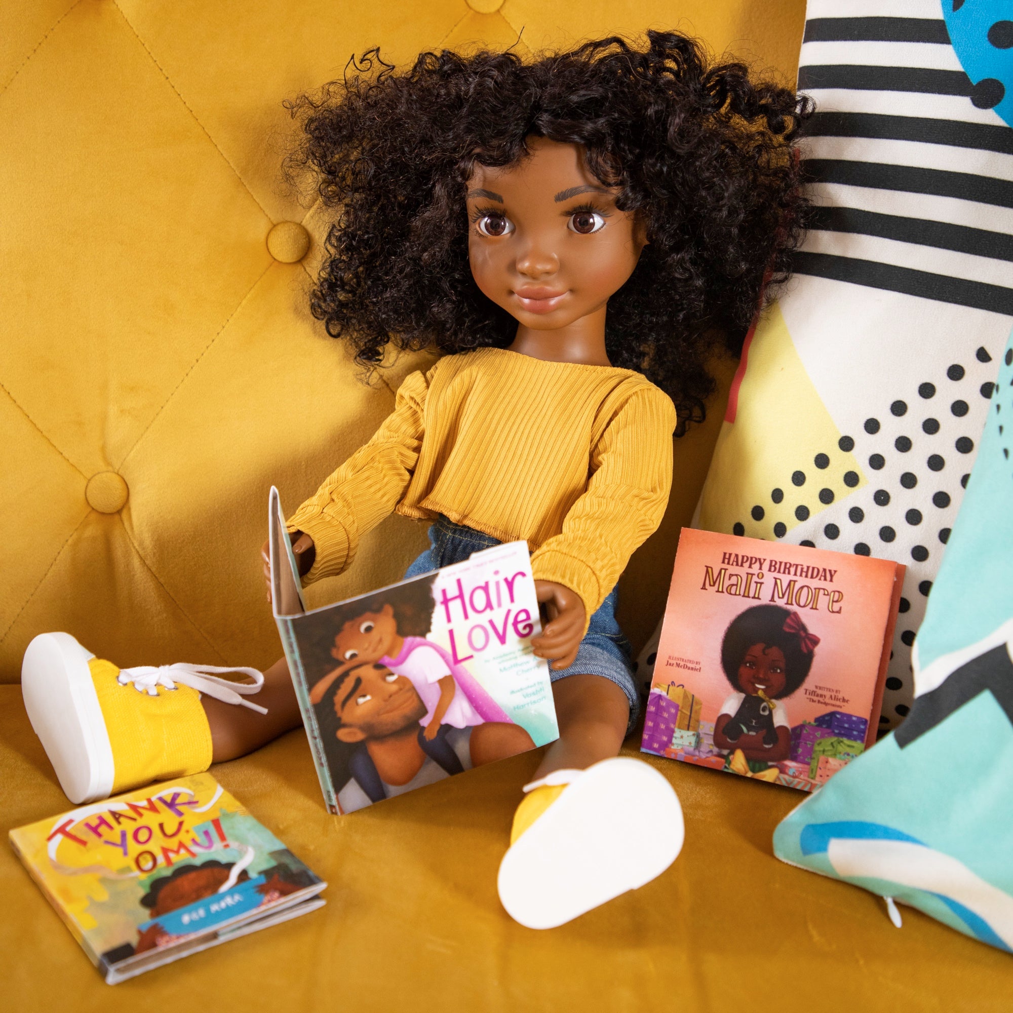 Healthy Roots Doll Zoe sits on a yellow couch surrounded by kids' books