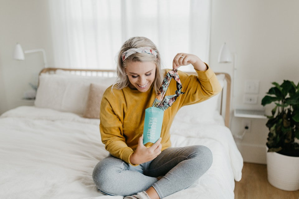 A model wearing a headband by Headbands of Hope while opening a package from the company. 