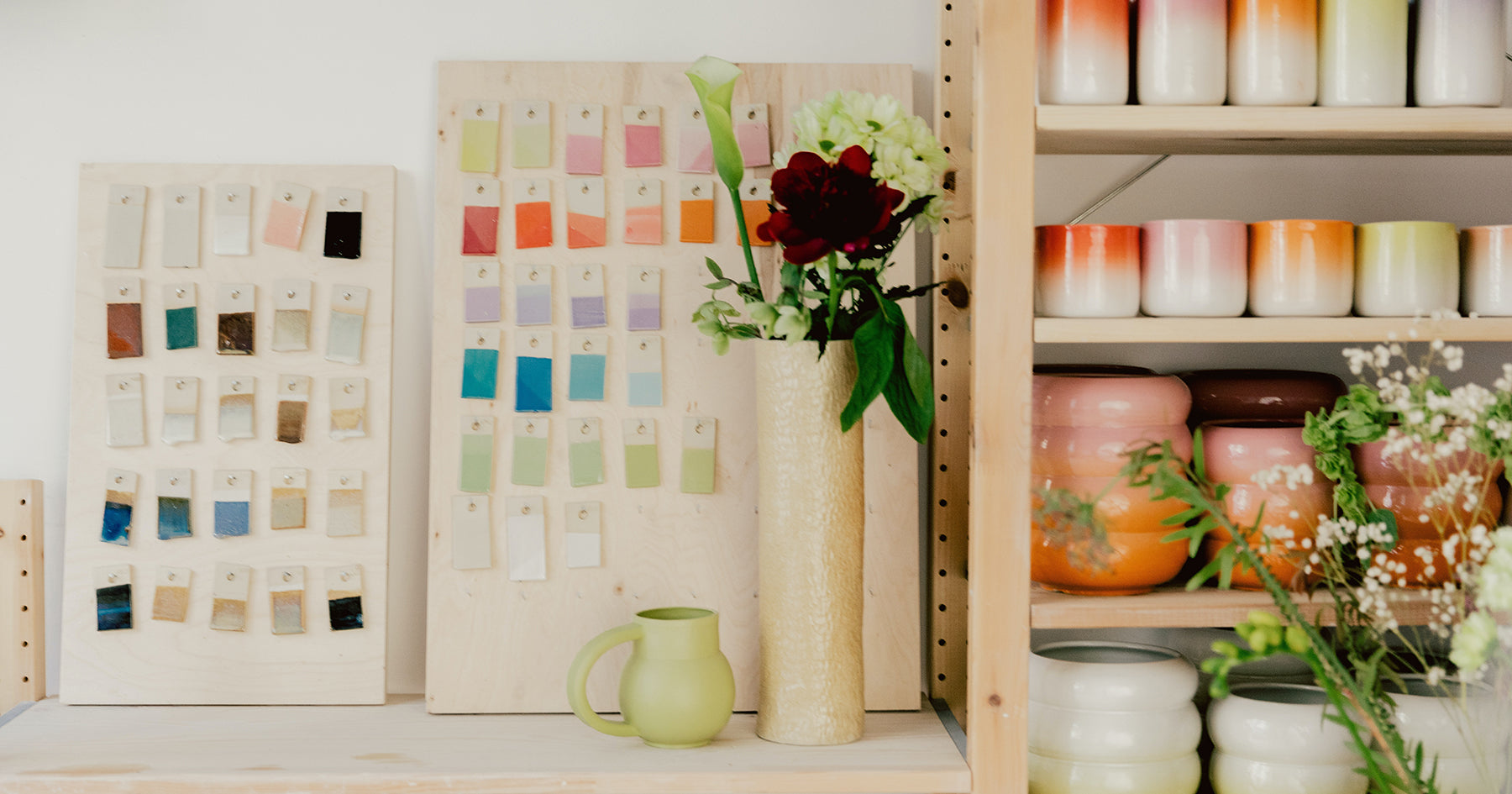 Inside an artist's studio, pottery sits on a tall shelf and colour samples lean against a wall