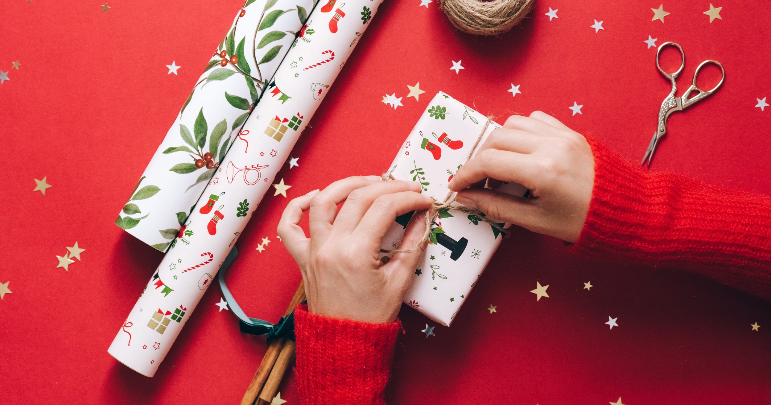 Two hands tie a bow on a Christmas present in a festive setting