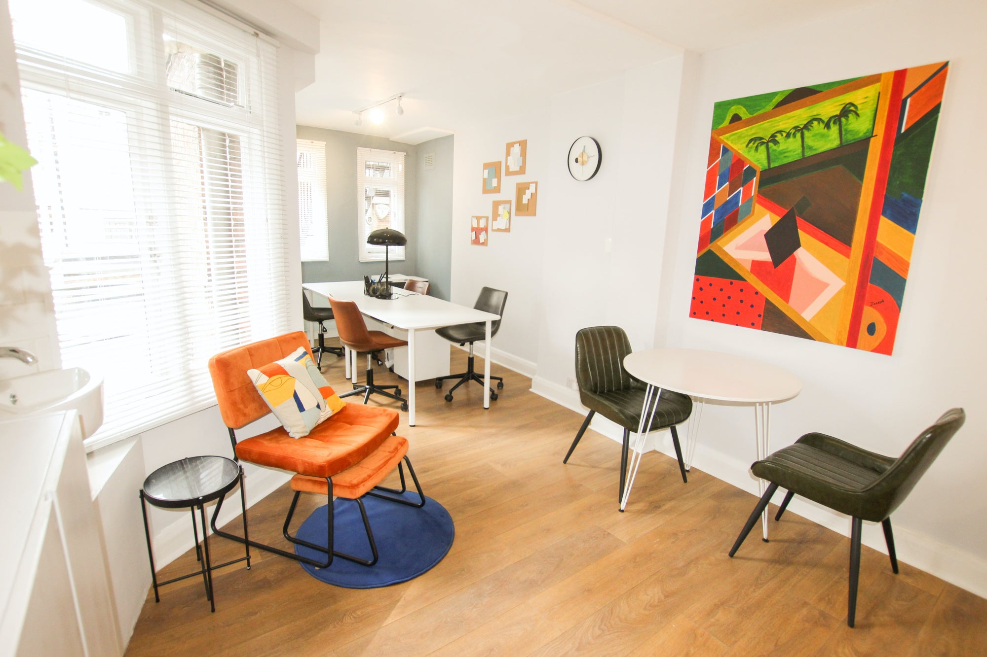 Wide shot of a living room with a dedicated workspace. A large piece of colorful art adorns the wall