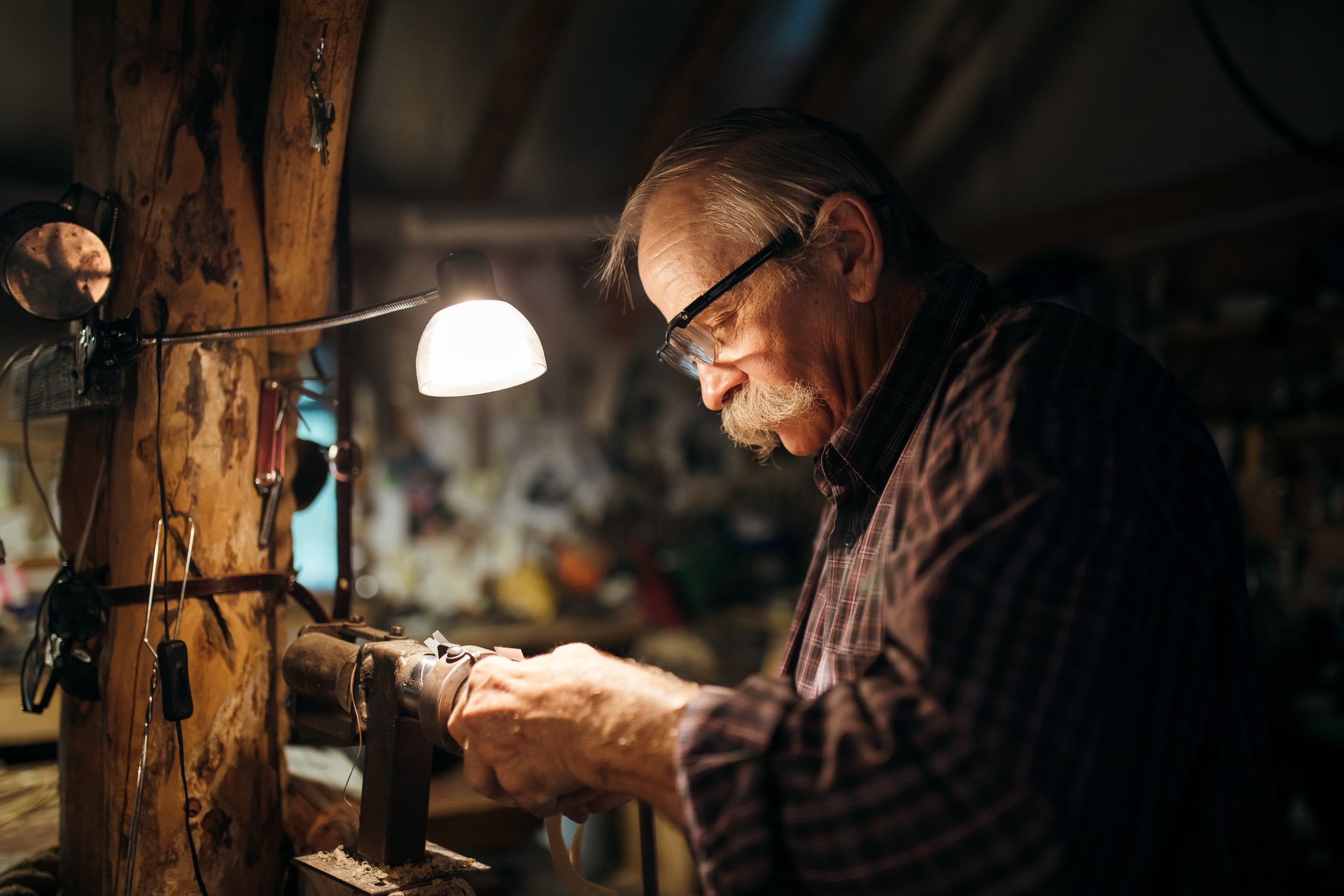 An older person works in a cozy workshop lit by a work light