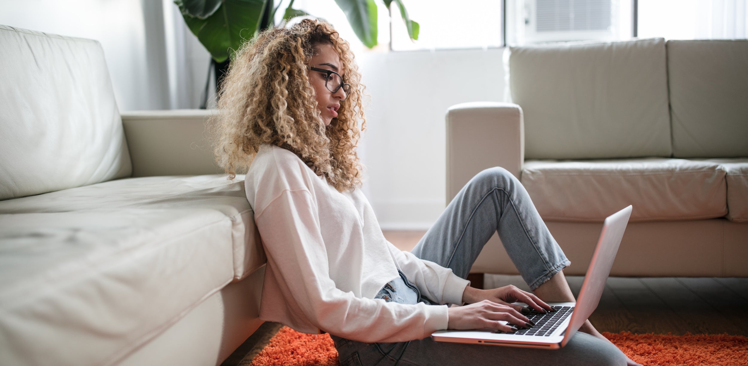 A person sits on the floor while typing on their laptop