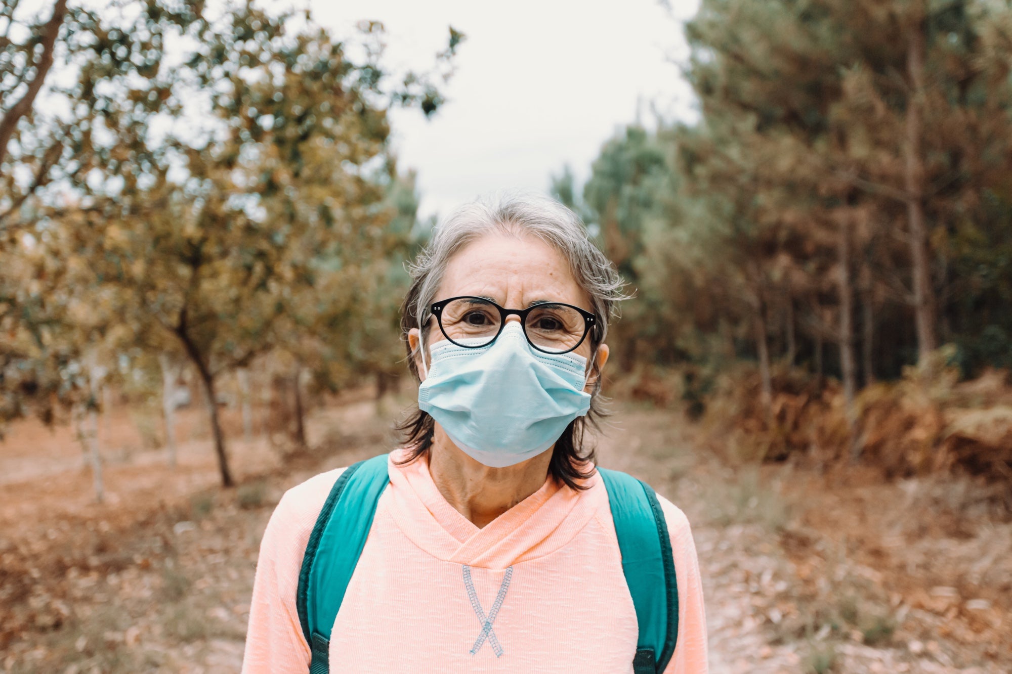 A person wearing a face mask and backpack takes a hike in the woods