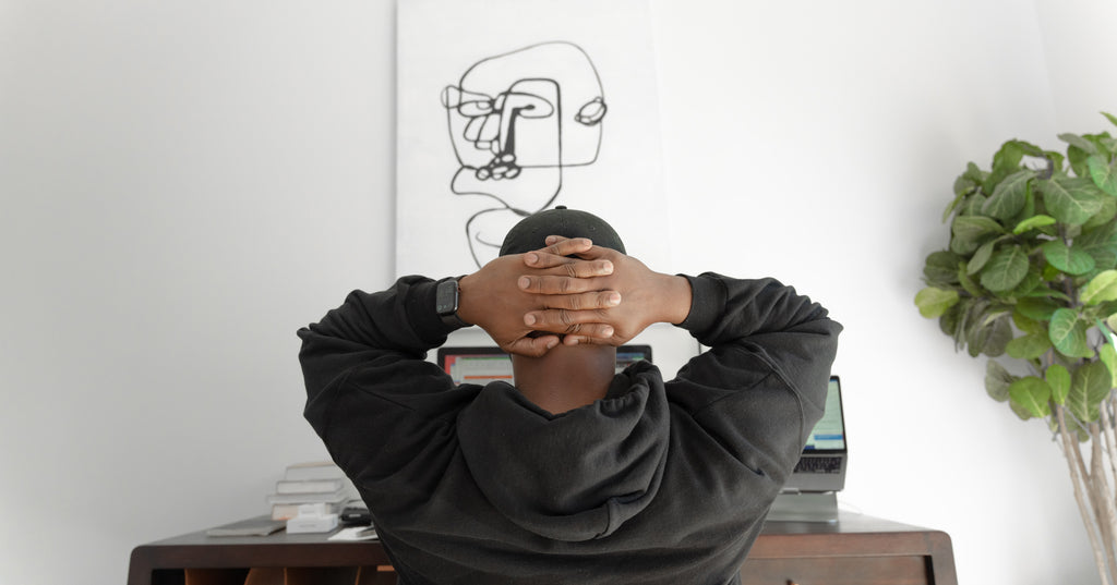 Person photographed from behind holds their head while sitting at a desk